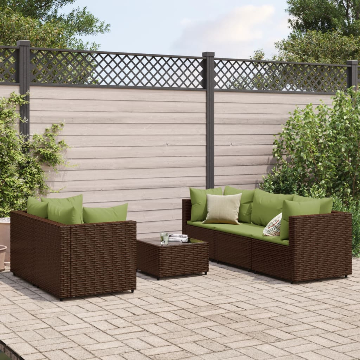 Garten-Terrassenset mit braunen Korbmöbeln, grünen Kissen und einem kleinen Tisch. Im Hintergrund ein Zaun und Blätter.
