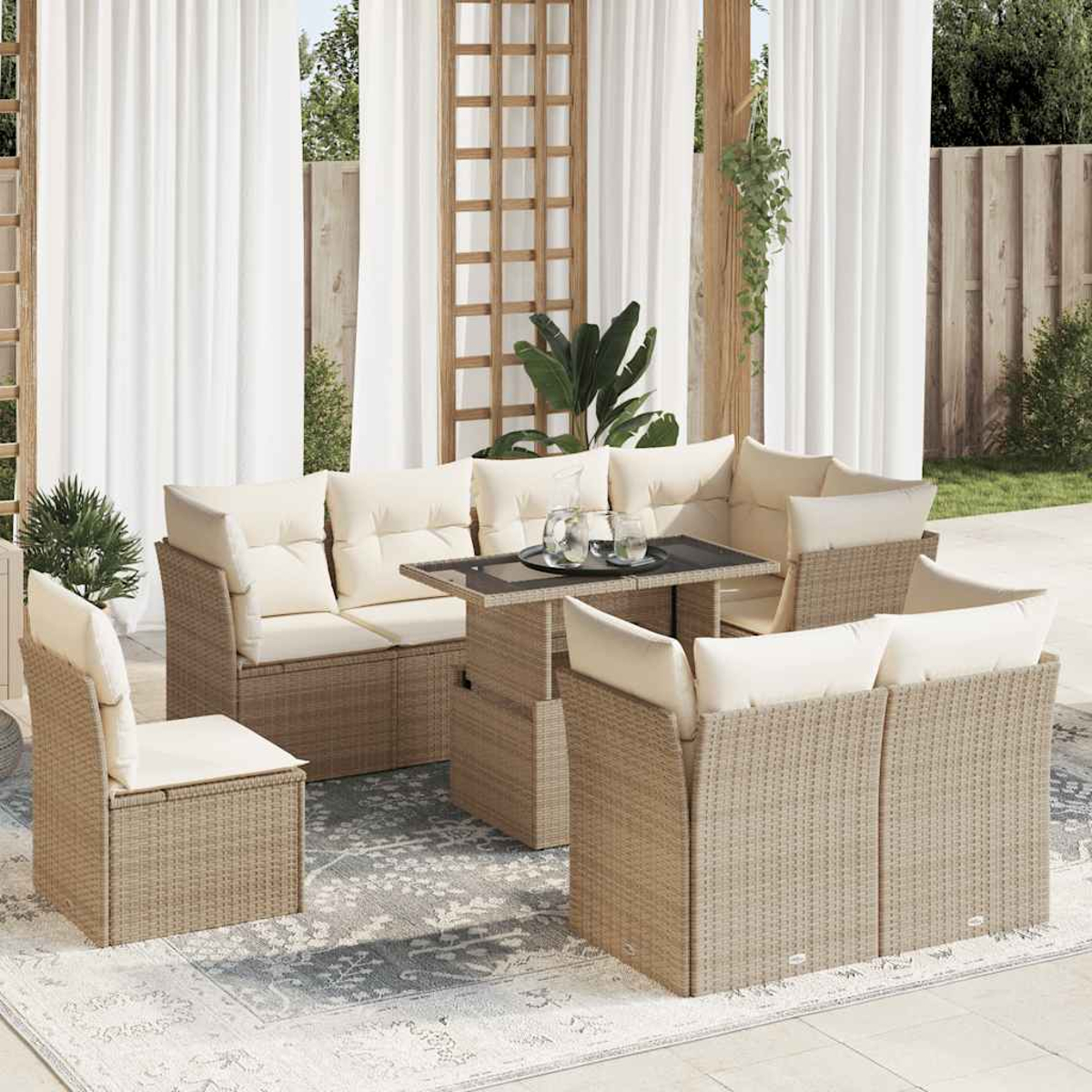 Set di mobili da esterno in rattan con cuscini color crema. Include tavolo, sedie e divani. Sfondo: tende bianche e verde.