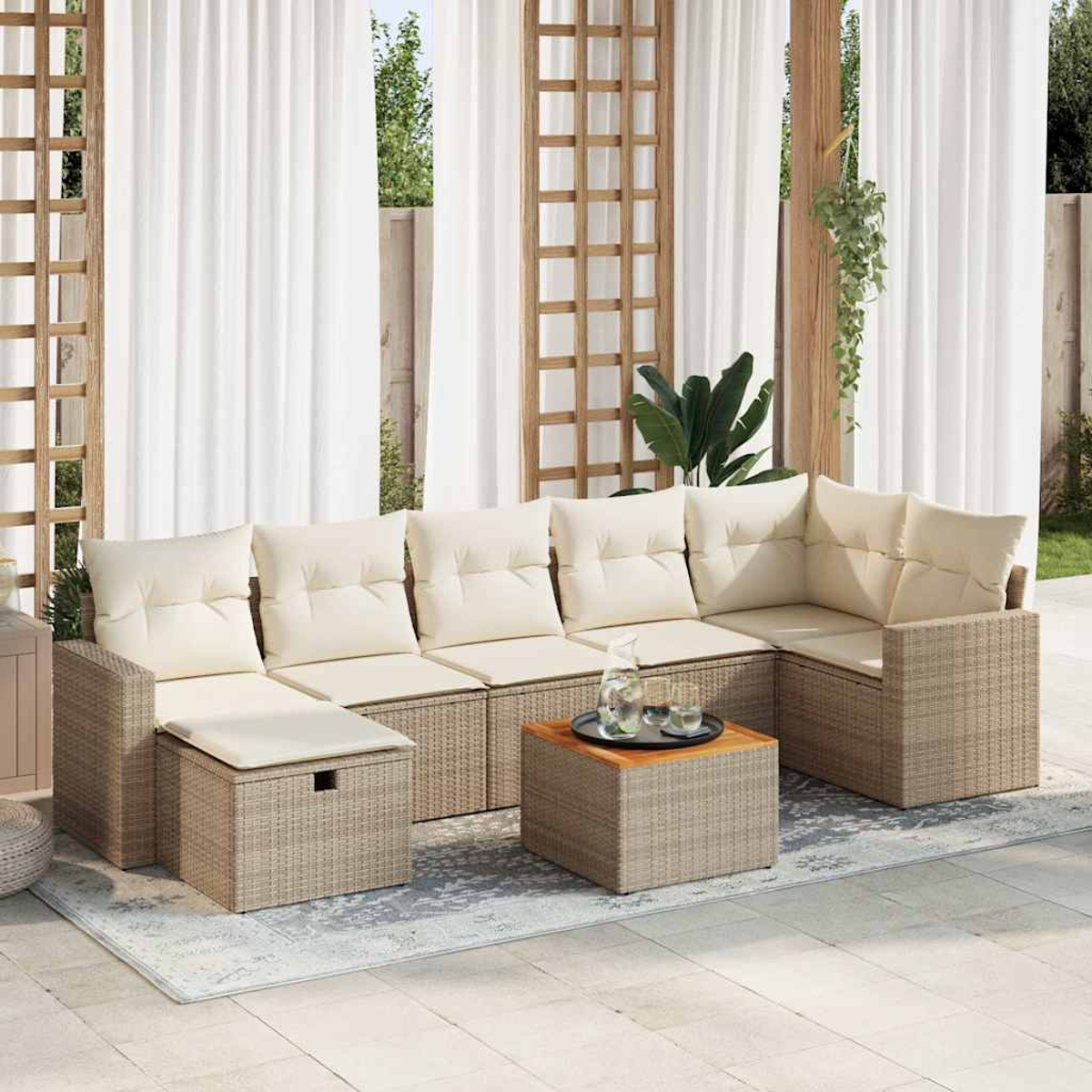 Set di sedute per esterni con cuscini beige, un tavolino in legno con bevande e tende bianche sullo sfondo.