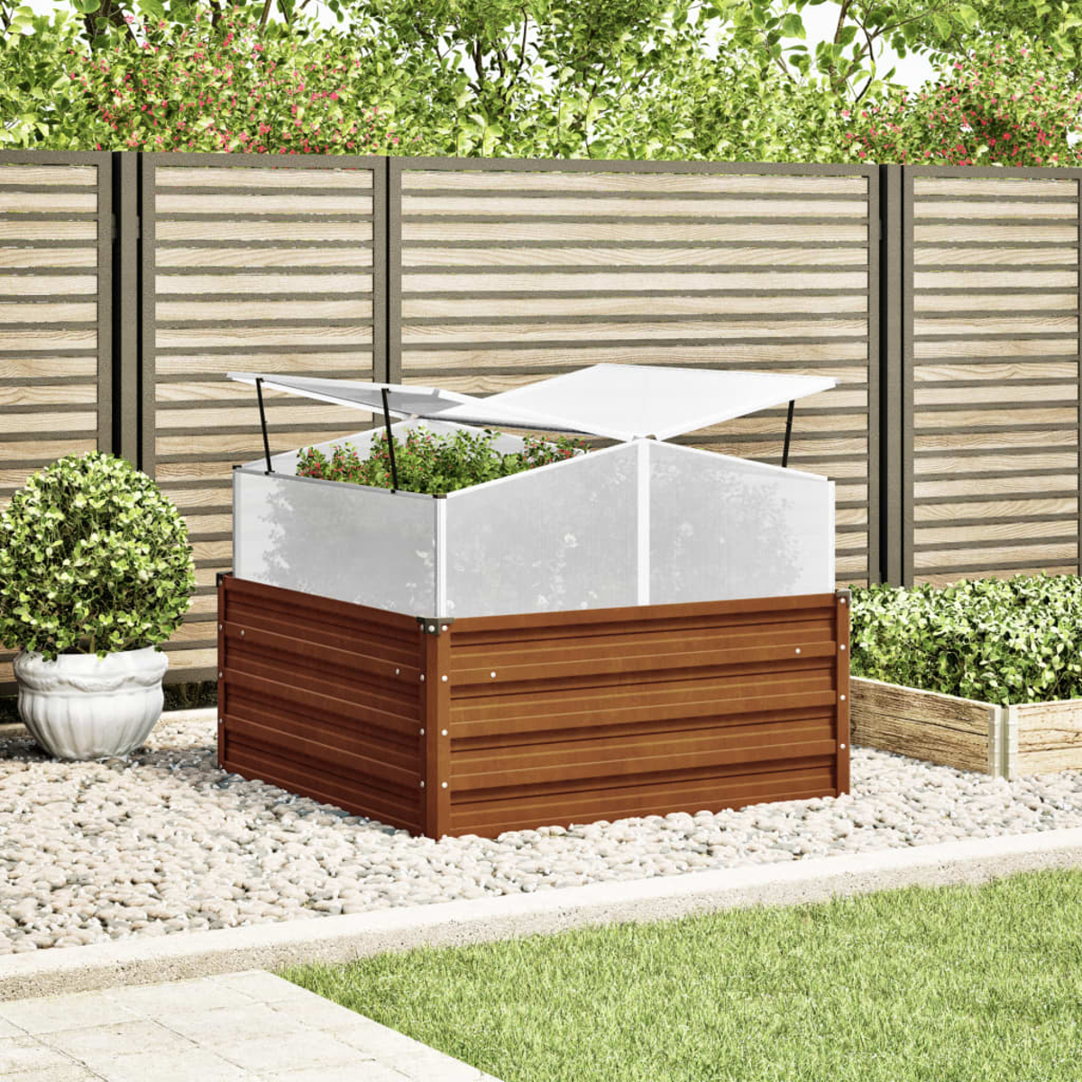 Un'aiuola rialzata con copertura trasparente. È in un giardino con piante, una recinzione di legno e pietre bianche.