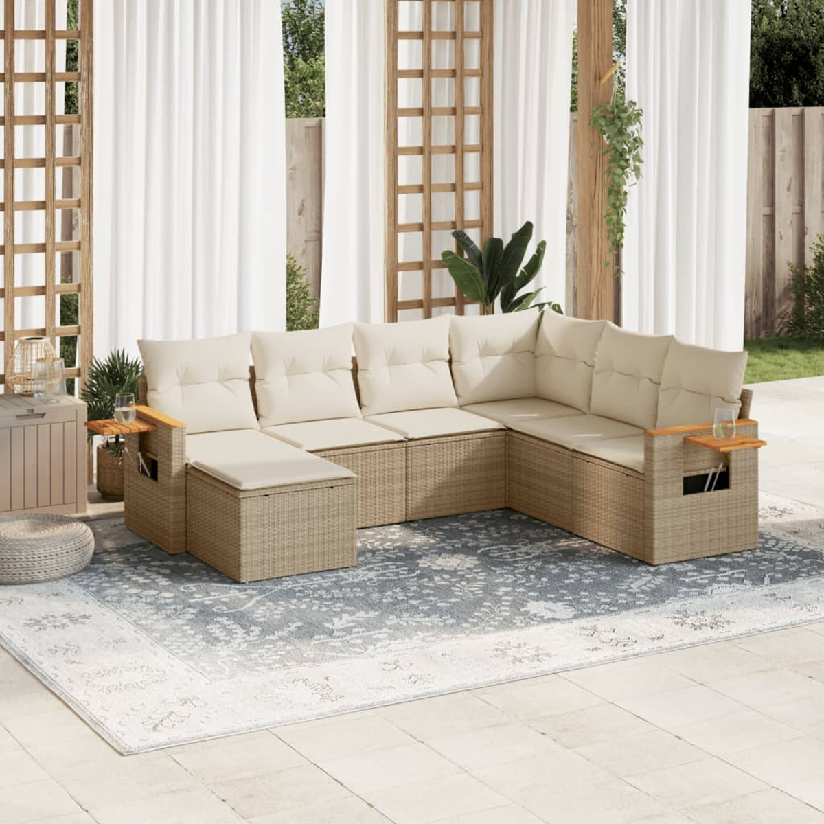 Patio esterno con divano componibile beige, cuscini e tavolini in legno. Un tappeto fantasia sul patio. Tende bianche sullo sfondo.