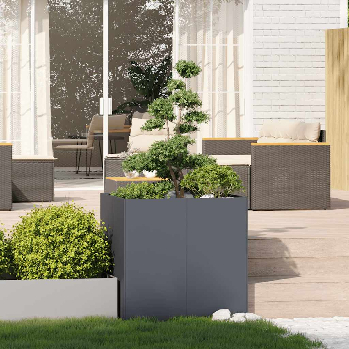Scena all'aperto con un bonsai in una fioriera grigia. Sullo sfondo, mobili da patio, tra cui un tavolo e sedie.