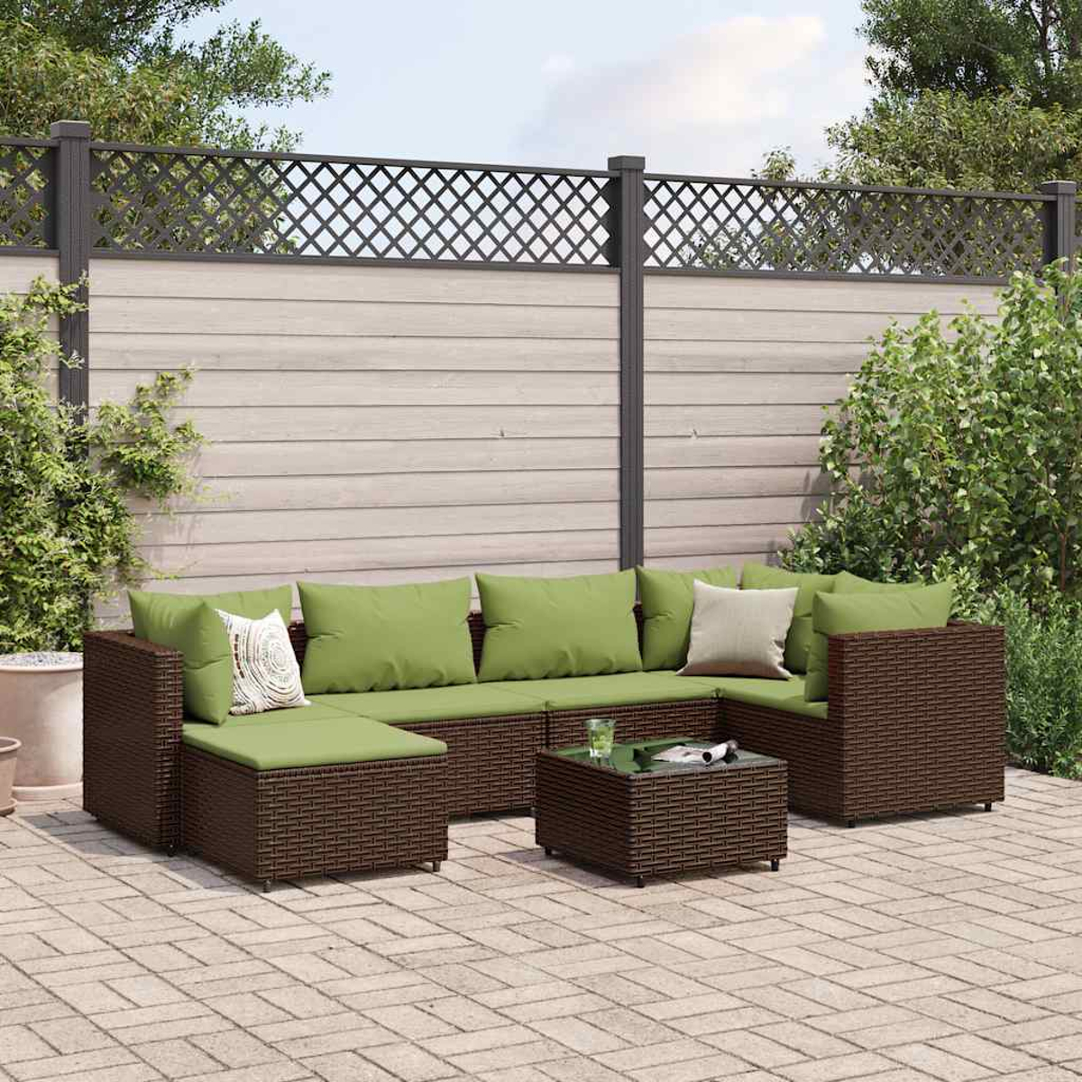 Divano in vimini da esterno con cuscini verdi su un patio in mattoni, un tavolino e una recinzione decorativa sullo sfondo.