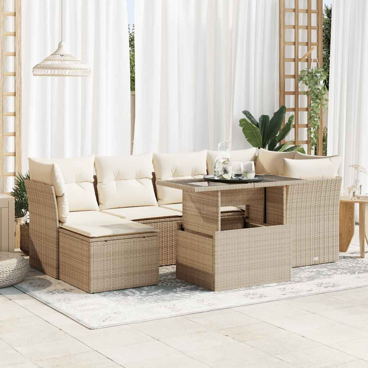 Rattan-Garnitur für draußen mit Kissen. Tisch mit Gläsern und Krug. Weiße Vorhänge im Hintergrund.