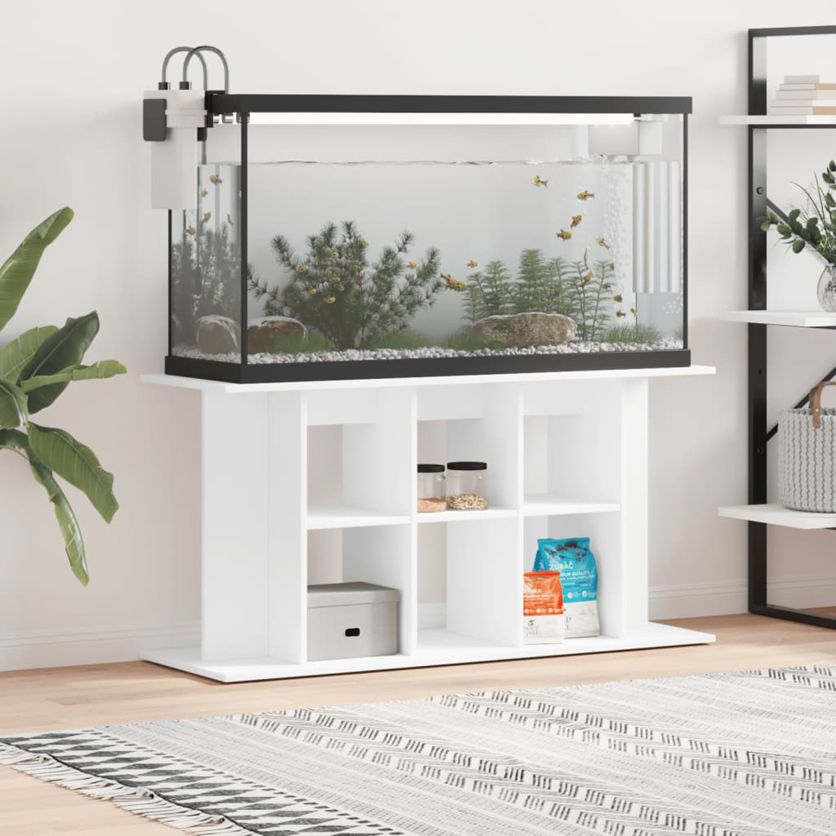 Ein weißer Aquarienstand mit einem Aquarium darauf, das Fische, Pflanzen und Steine enthält. Regale darunter halten Vorräte.