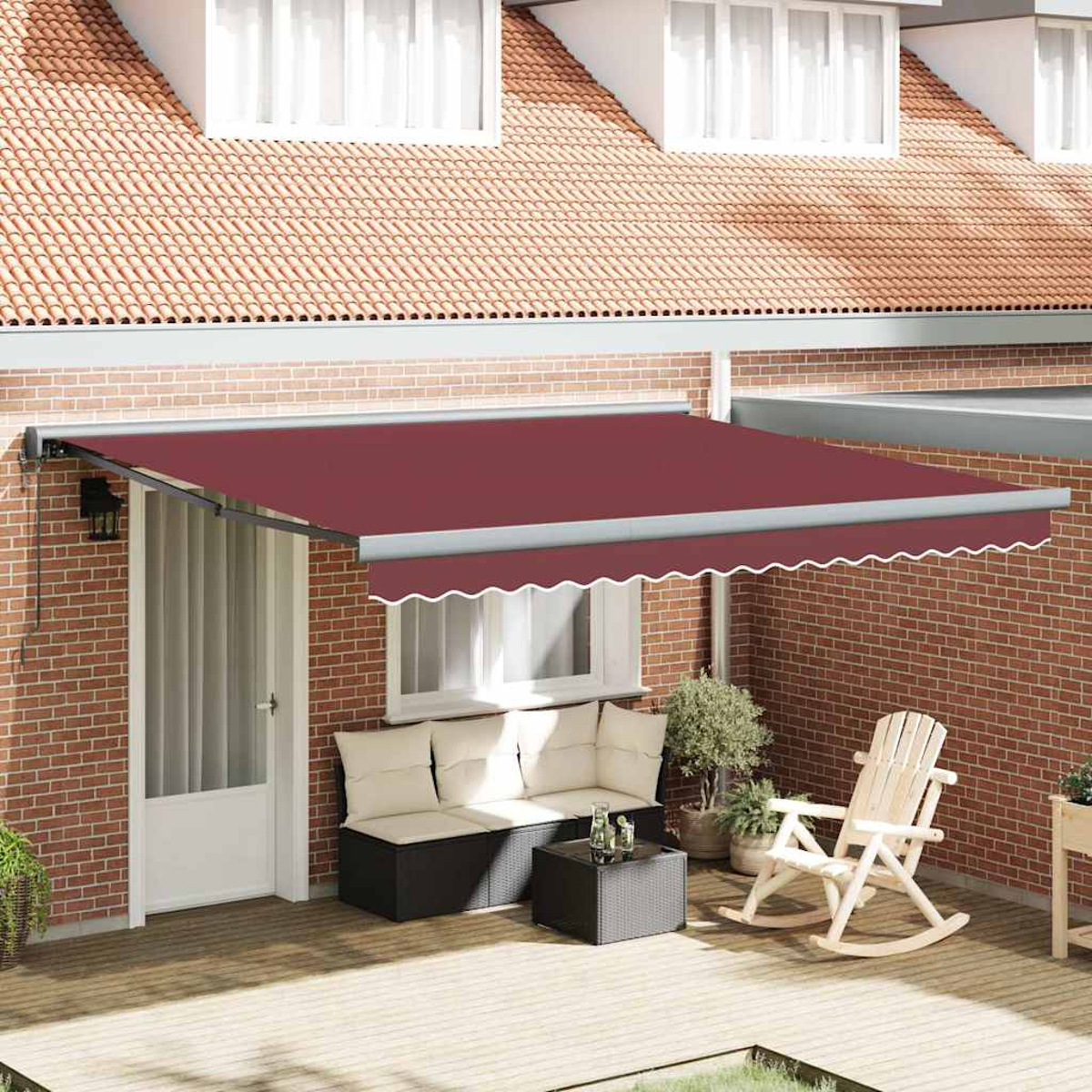 Una tenda da sole bordeaux si estende da un muro di mattoni. Sotto, un patio comprende un'area salotto con divano, tavolo e sedia a dondolo.