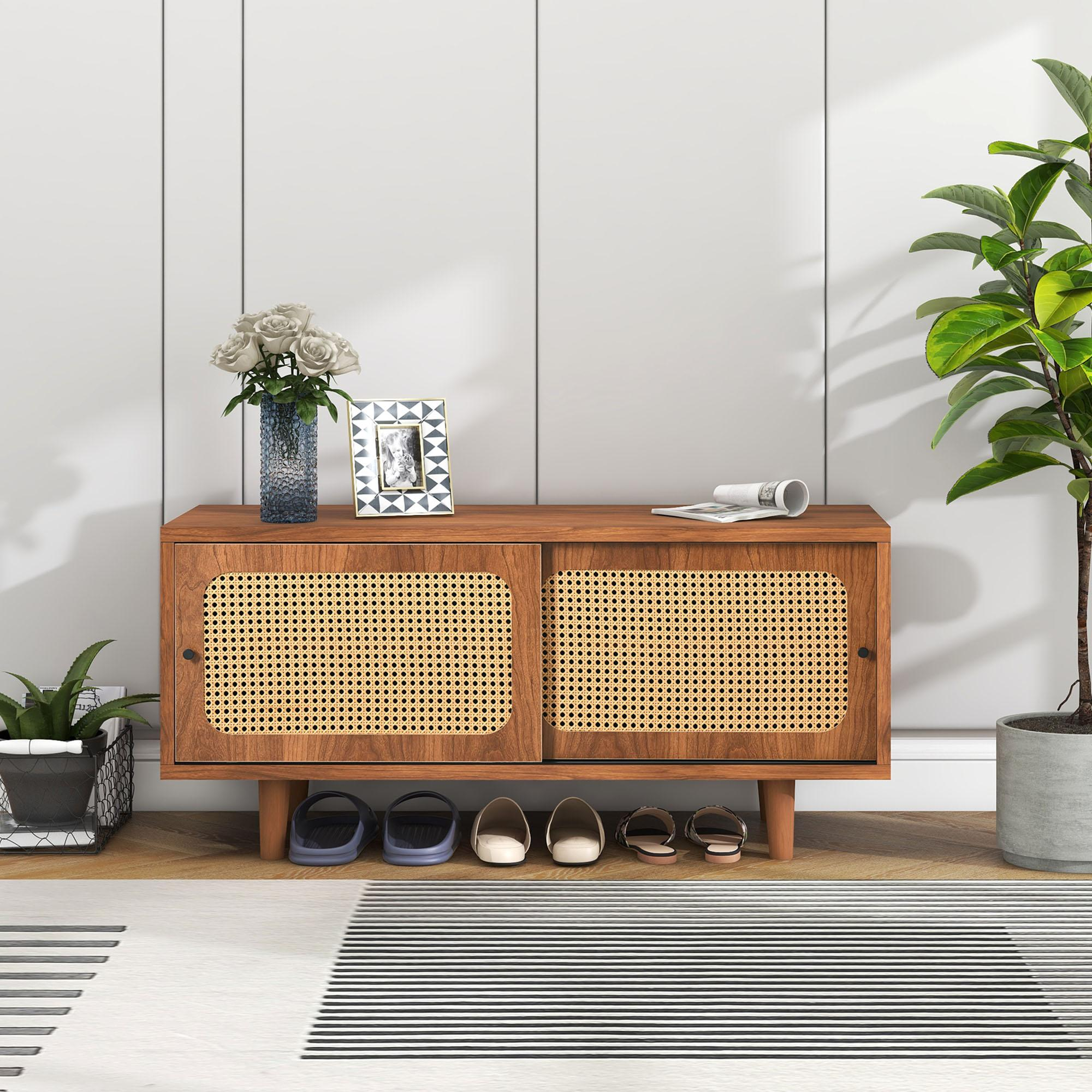 Ein Holzschrank mit Rattantüren, Schuhen, Blumen und einer Pflanze vor einer weißen Wand.