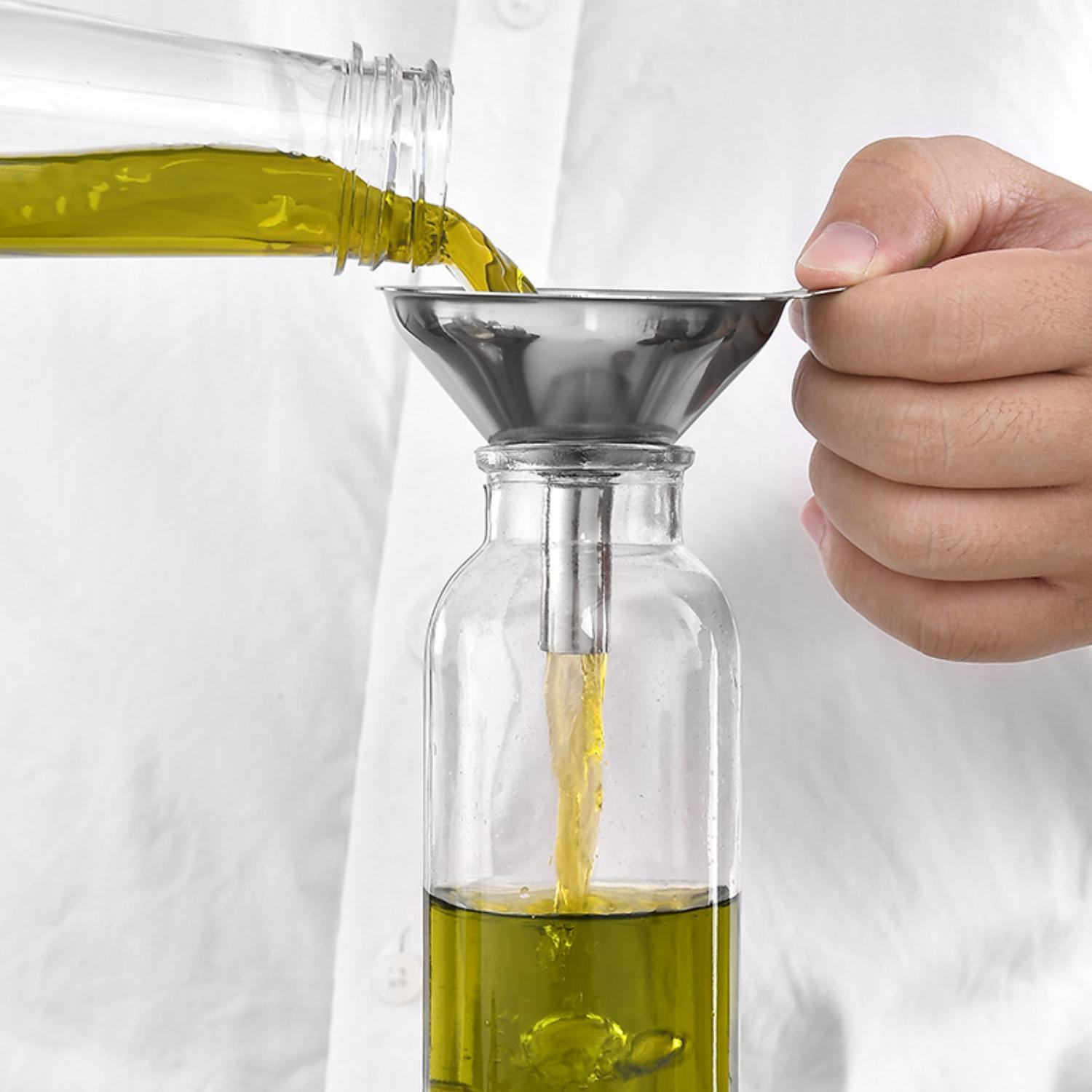 Eine Person gießt Olivenöl aus einer Flasche mit einem Trichter in eine Glasflasche. Das Öl ist gelbgrün.
