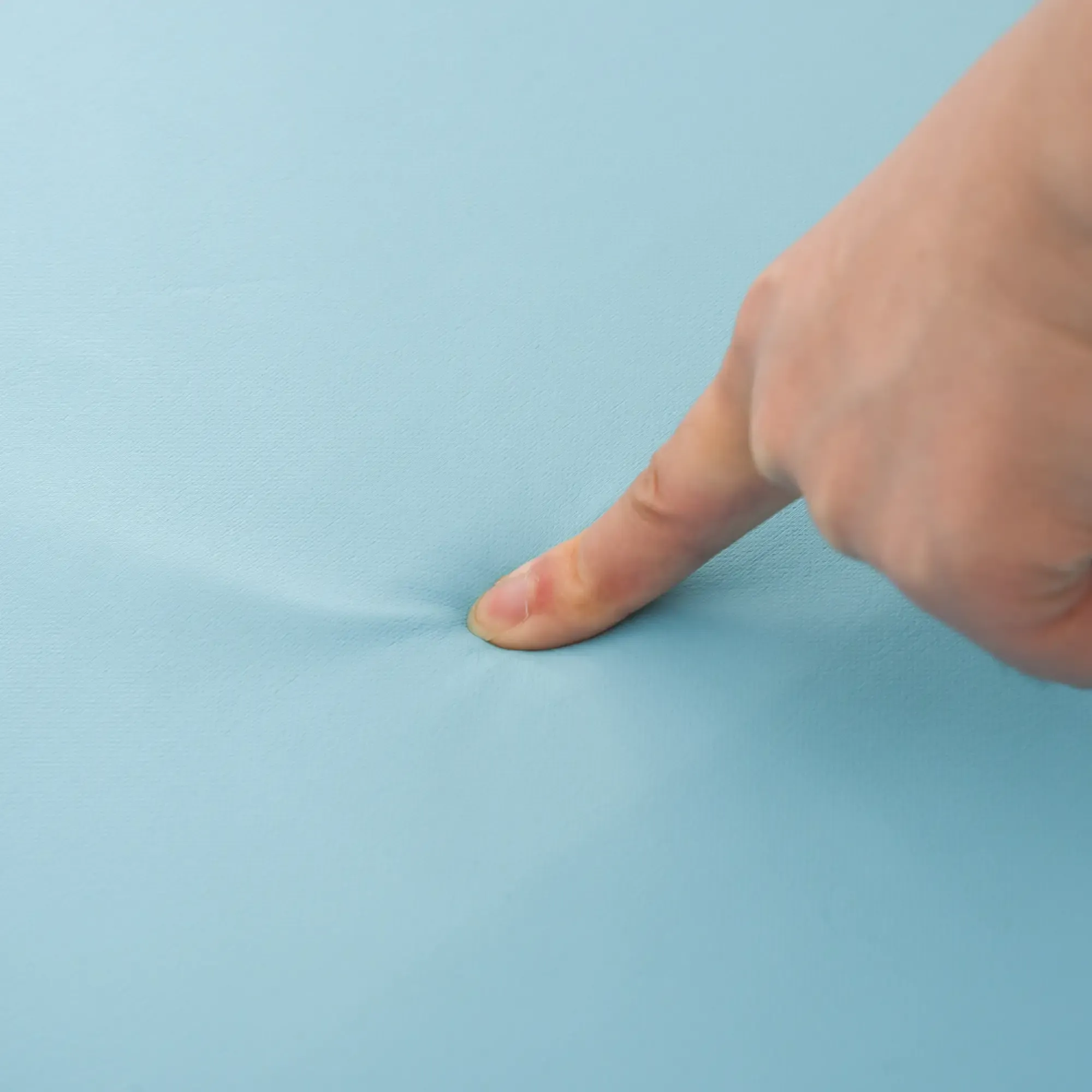 Ein Finger drückt auf eine hellblaue Oberfläche und erzeugt eine kleine Vertiefung. Der Finger ist fleischfarben.