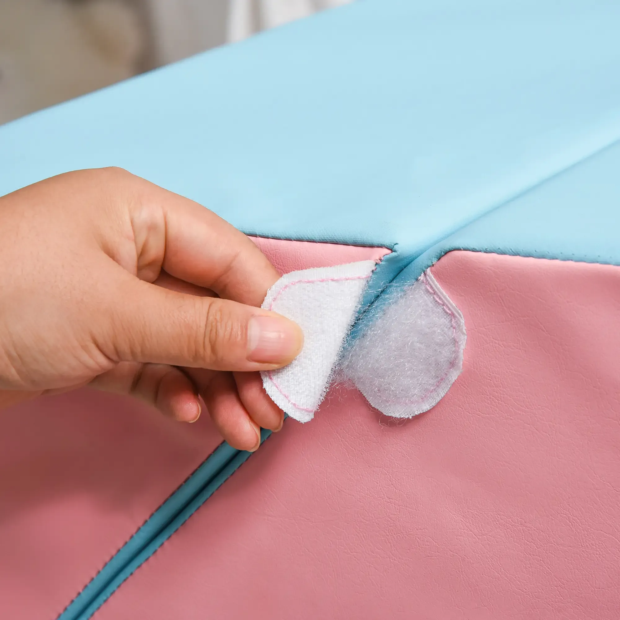 Eine Hand löst Klettverschluss auf einer rosa und blauen Oberfläche. Die Oberfläche scheint ein weiches Material zu sein.