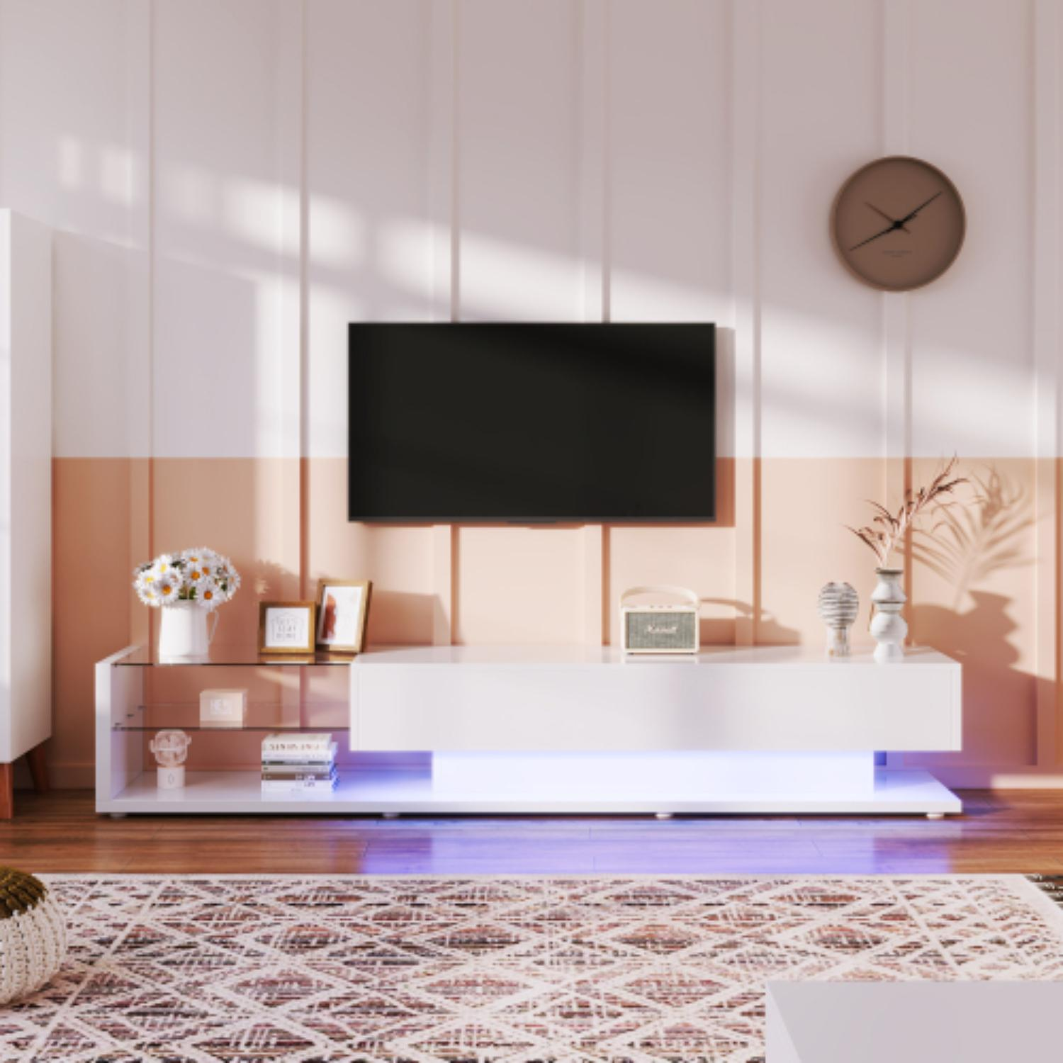 Wohnzimmer mit weißem TV-Ständer, Fernseher, Uhr und Blumen. Die Wand ist weiß und pfirsichfarben, der Boden ist aus Holz.