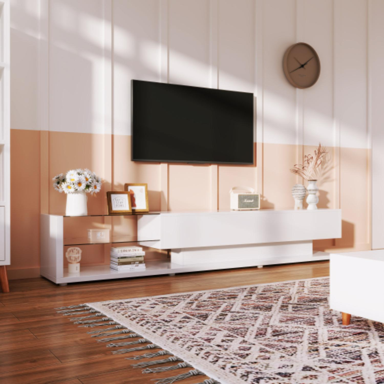Ein Wohnzimmer mit einem Fernseher auf einem weißen Schrank. Ein Teppich und eine Uhr sind ebenfalls vorhanden. Eine Vase mit Blumen steht auf dem Schrank.