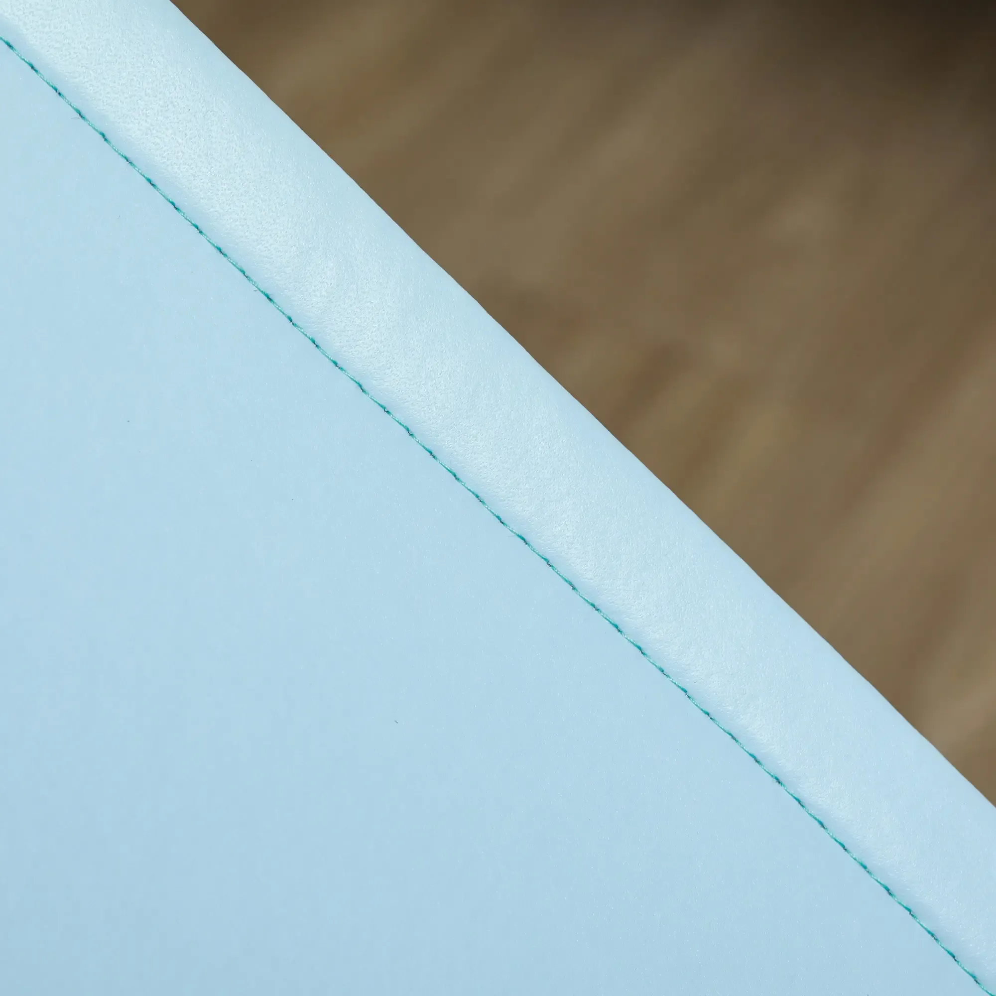 Eine hellblaue Oberfläche mit grünen Nähten diagonal durch den Rahmen. Im Hintergrund befindet sich eine braune Holzoberfläche.