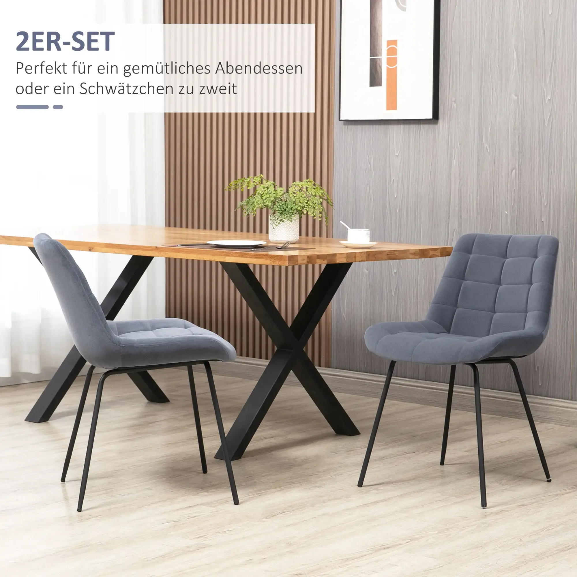 Eine Esstischszene mit Holztisch, zwei grauen Stühlen und einer Pflanze. Der Hintergrund ist eine neutrale Wand mit Kunst.