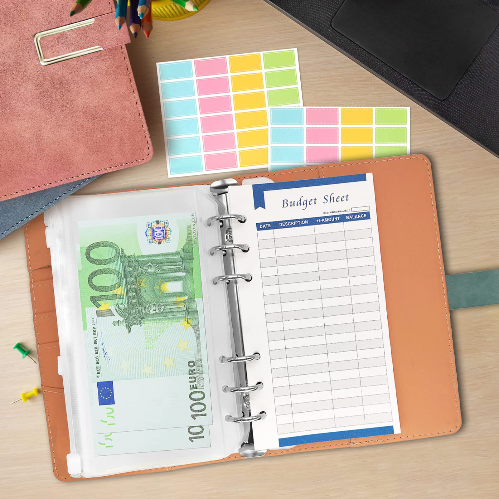 Ein Budgetblatt mit einem 100-Euro-Schein in einem Ordner, bunte Haftnotizen, ein rosa und blaues Notizbuch auf einer Holzoberfläche.