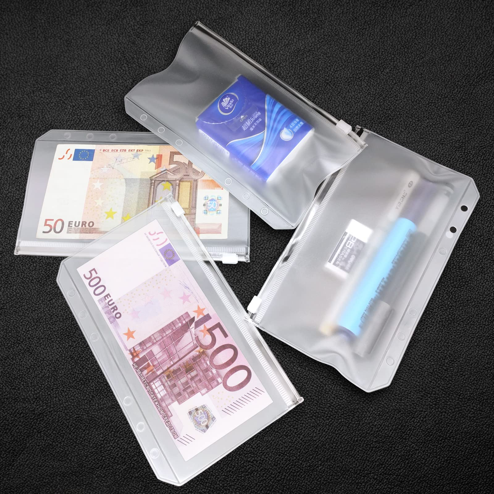 Das Bild zeigt transparente Beutel mit Bargeld, Taschentüchern und Schreibwaren auf einer schwarzen, strukturierten Oberfläche.