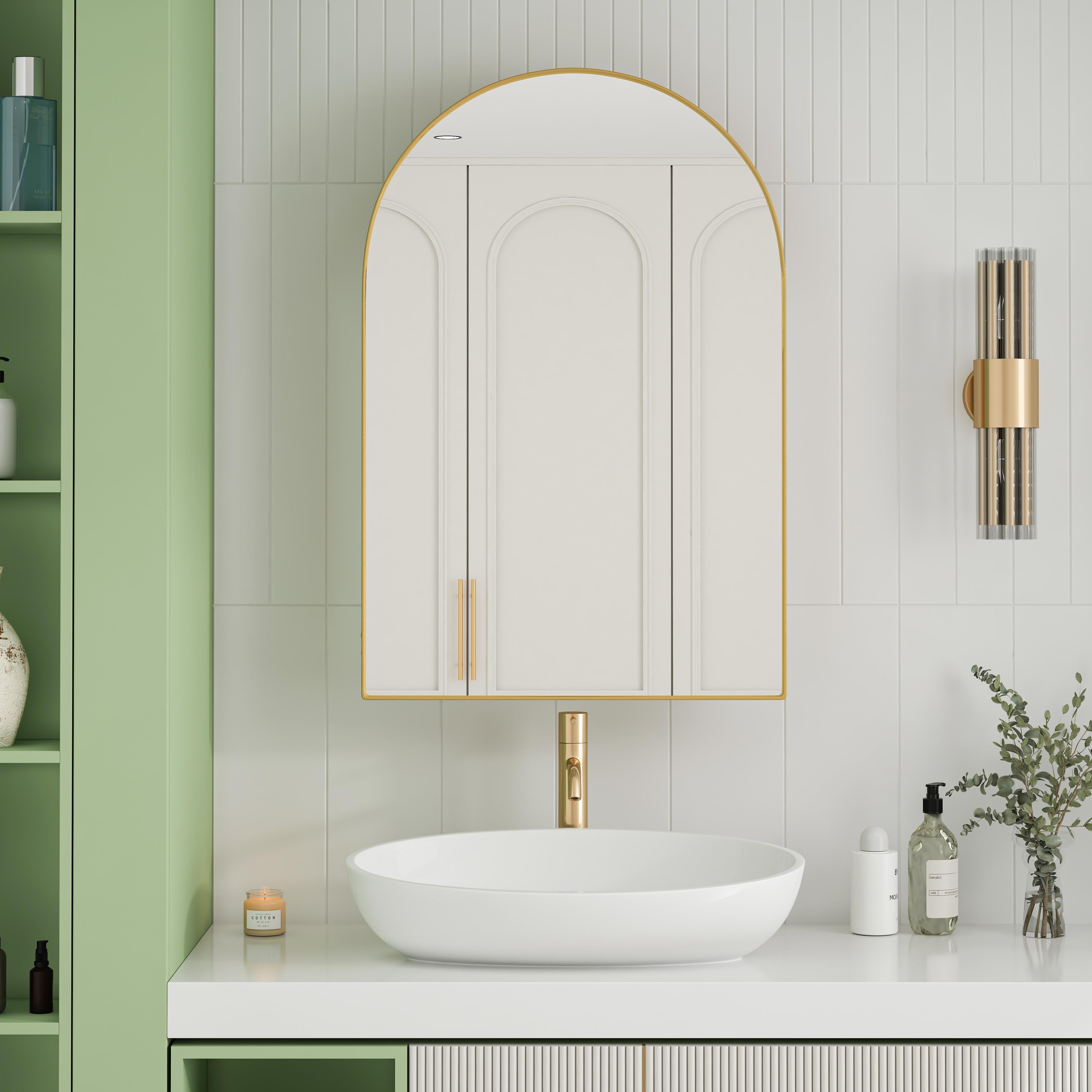 Ein Badezimmer mit weißem Waschbecken, Spiegel und Wand. Grüne Schränke links. Kerze und Seifenflaschen auf der Theke.