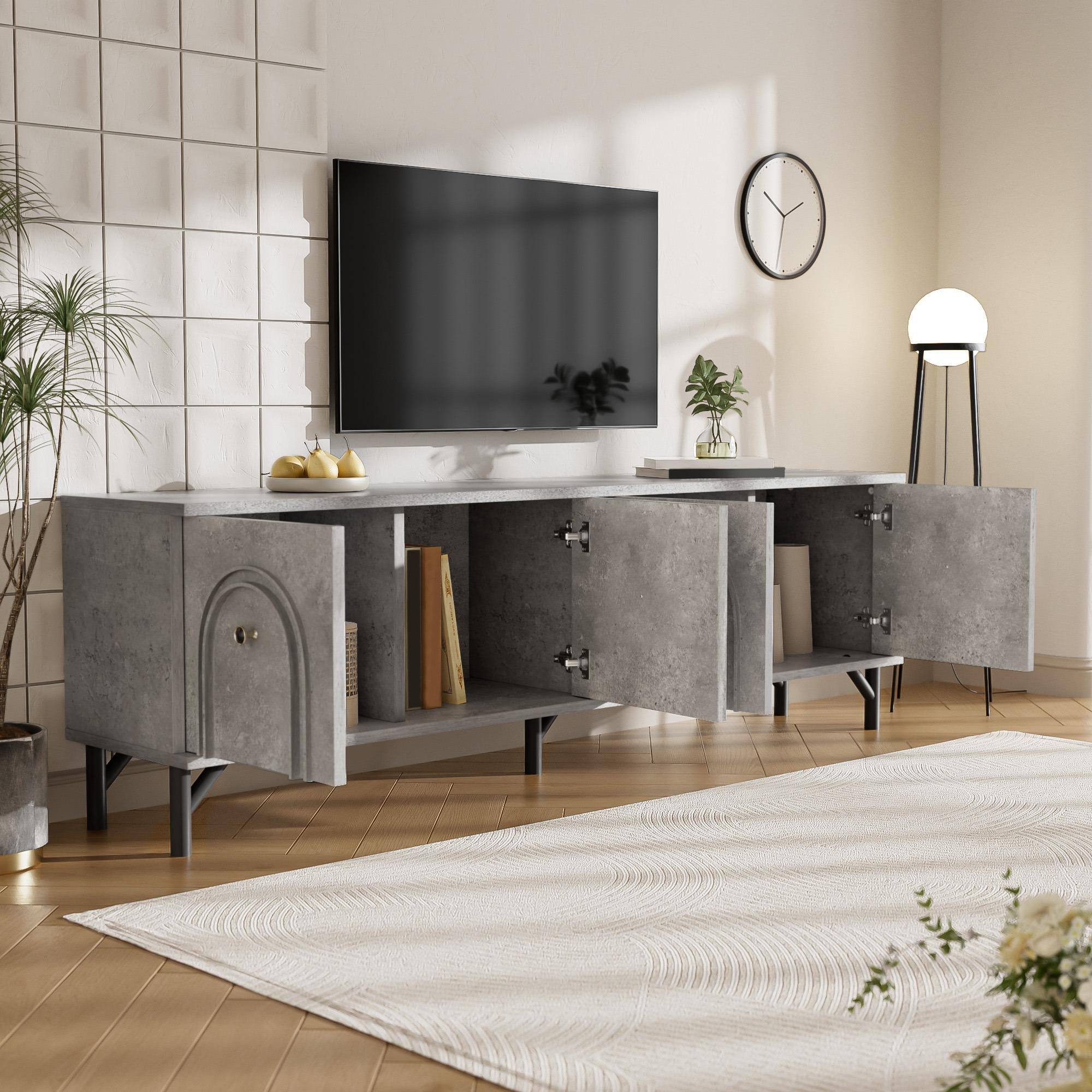 Ein modernes Wohnzimmer mit Fernseher auf einem grauen Schrank. Bücher, Pflanzen und eine Uhr sind sichtbar. Ein Teppich und eine Stehlampe sind ebenfalls vorhanden.