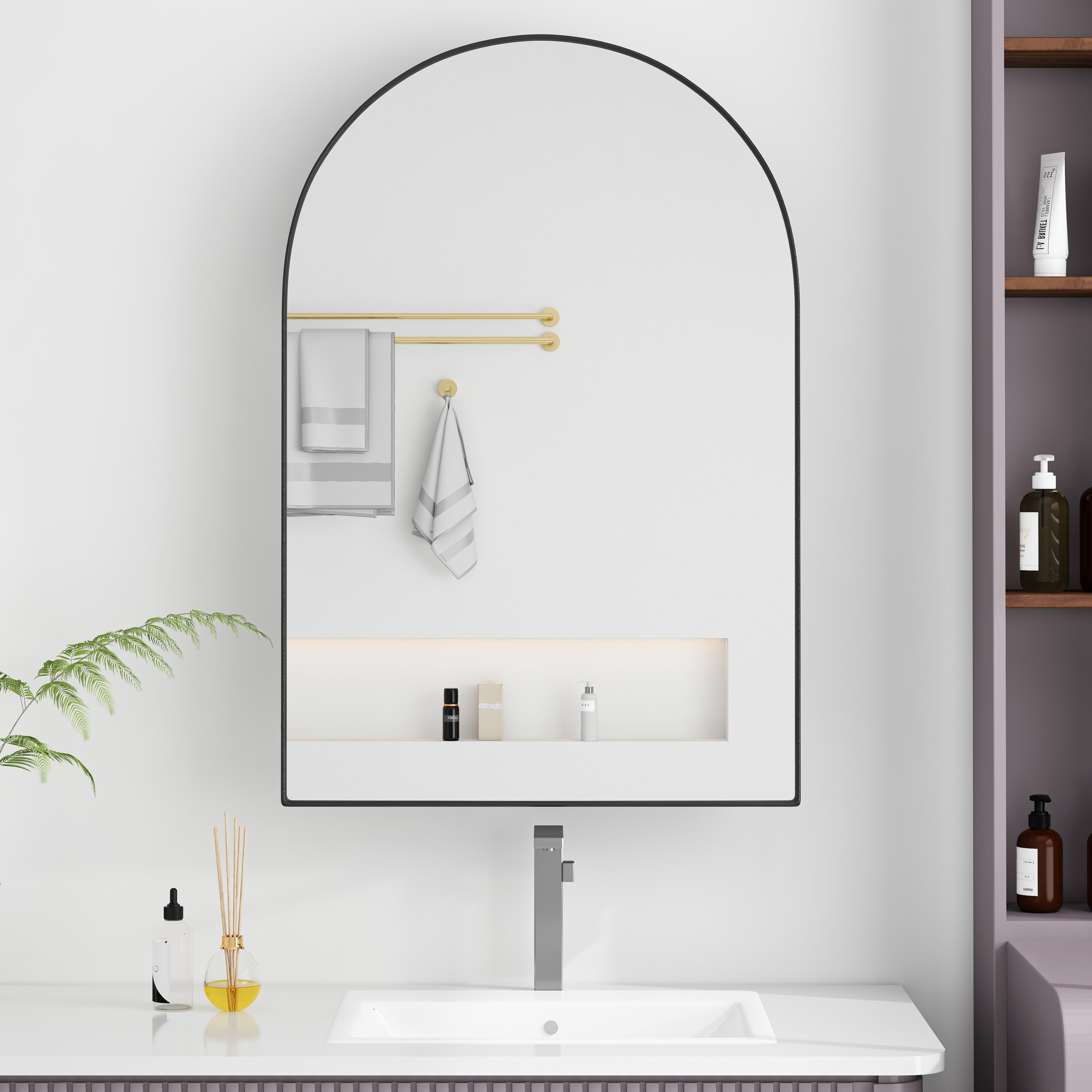 Ein Badezimmerspiegel mit Handtüchern, Waschbecken und Toilettenartikeln. Ein Regal rechts hält Flaschen. Eine Pflanze und ein Diffusor stehen auf der Theke.