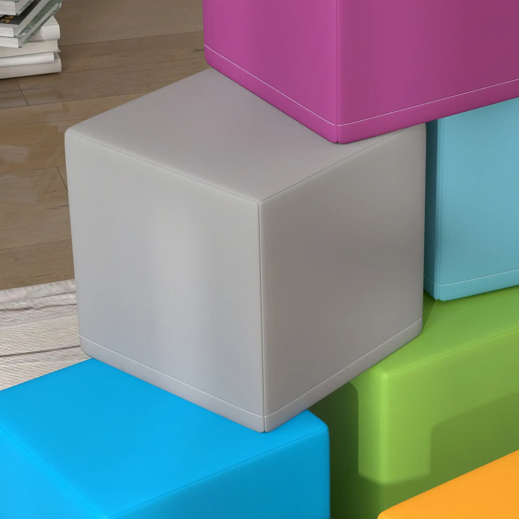 Gestapelte bunte Würfel. Grauer Würfel oben, Magenta, Blau, Grün und orange Würfel unten. Bücher im Hintergrund.