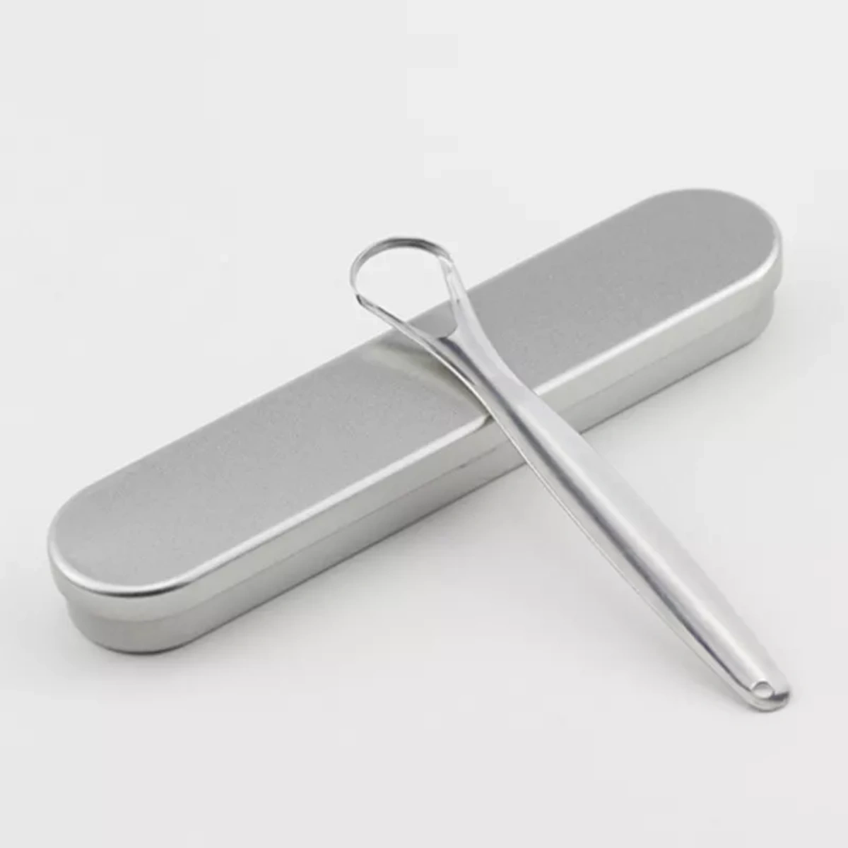 Ein silberner Zungenschaber liegt neben einem passenden Etui, vor einem weißen Hintergrund. Der Schaber ist glänzend, das Etui matt.