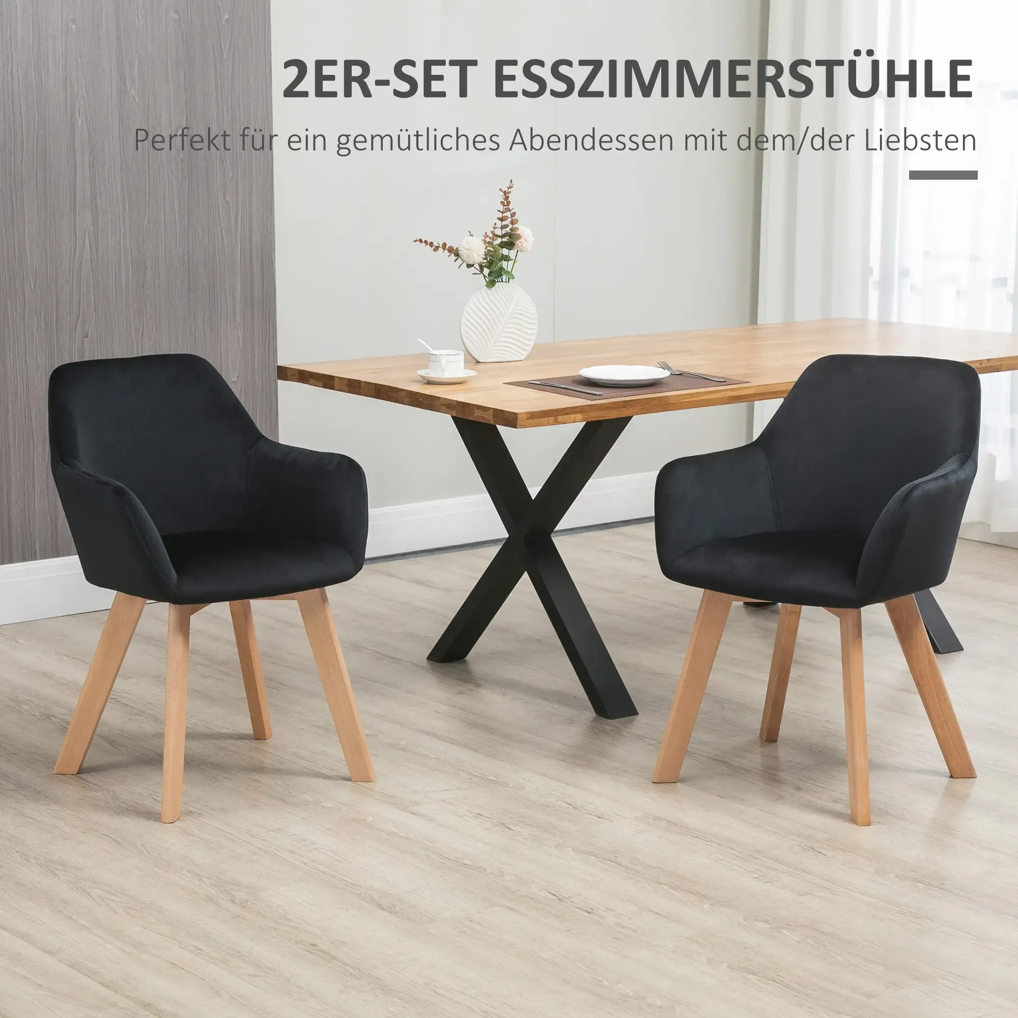 Zwei schwarze Sessel mit Holzbeinen stehen vor einem Holztisch. Auf dem Tisch steht eine Vase mit Blumen.