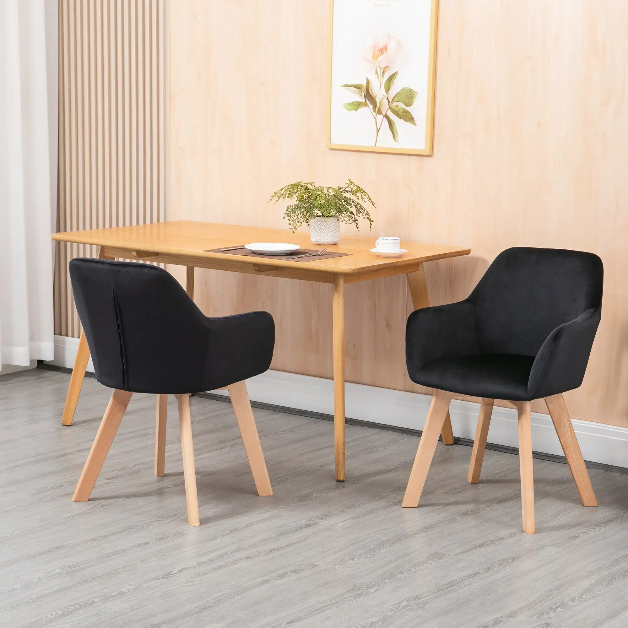 Esszimmer mit Holztisch, zwei schwarzen Stühlen, einem gerahmten Blumendruck und einer Pflanze.