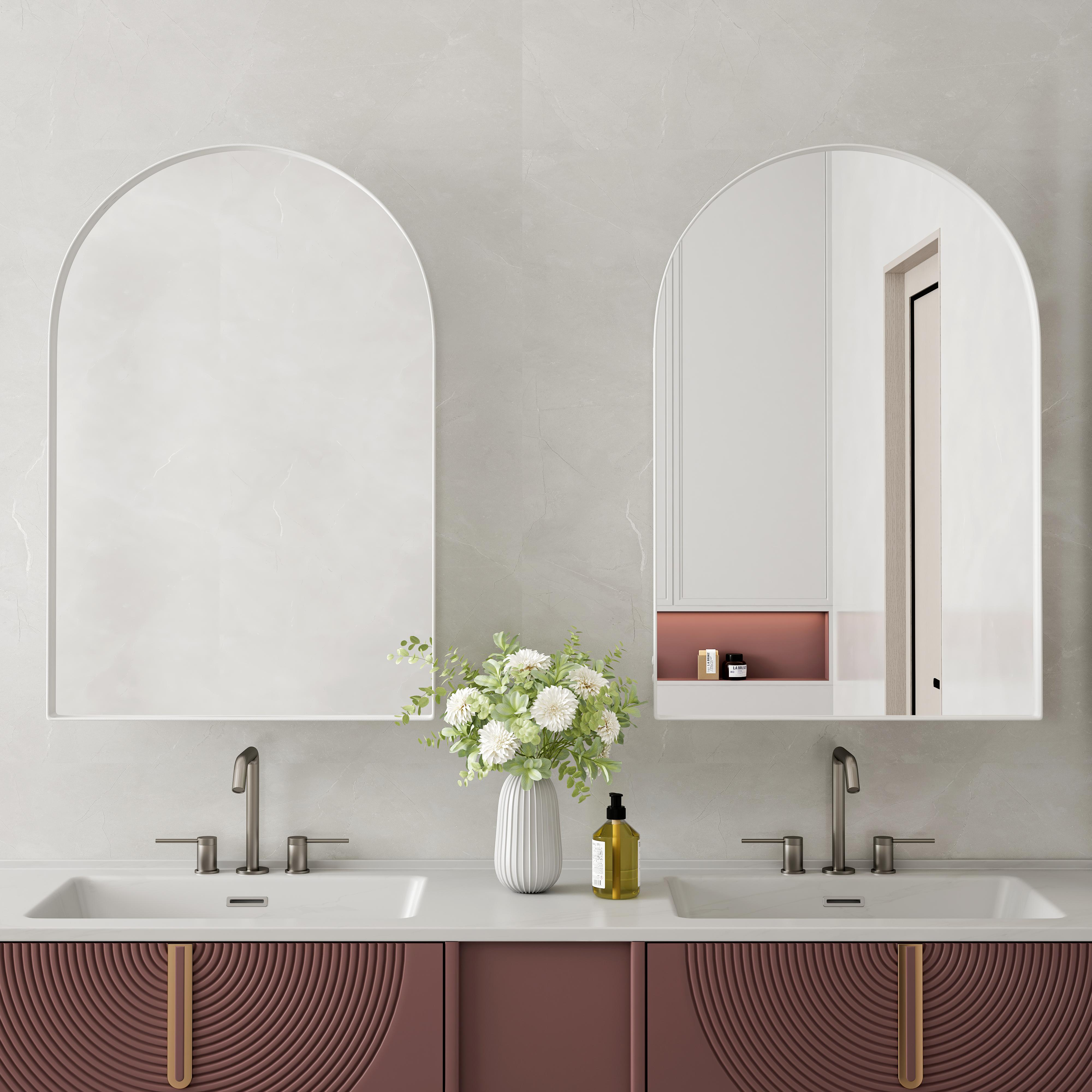 Badezimmer mit zwei Waschbecken, gewölbten Spiegeln und einer Vase mit Blumen. Darunter ein weinroter Schrank mit goldenen Griffen.