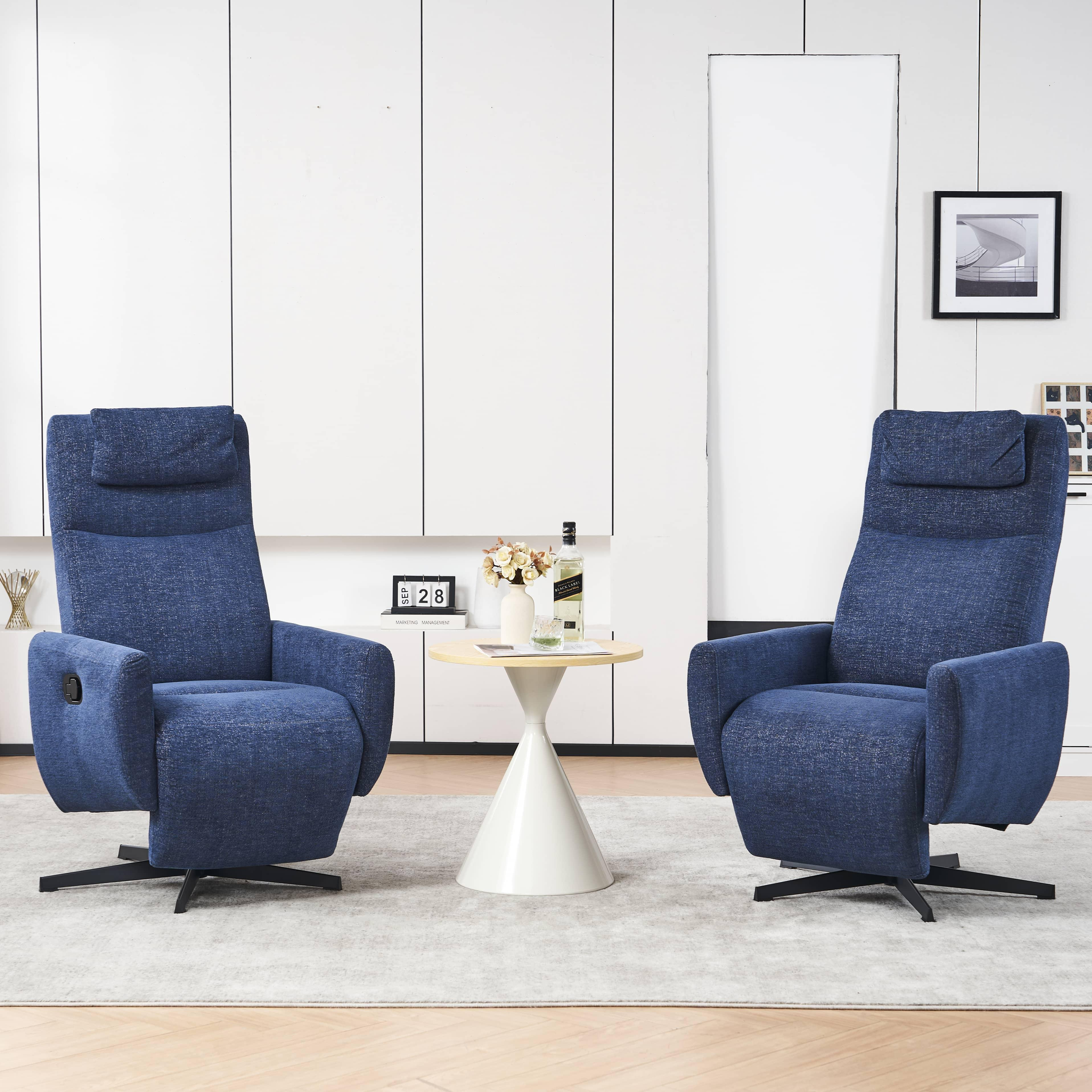 Zwei blaue Sessel stehen sich gegenüber. Zwischen ihnen steht ein kleiner Tisch mit Blumen und einer Flasche. Weisse Wand im Hintergrund.