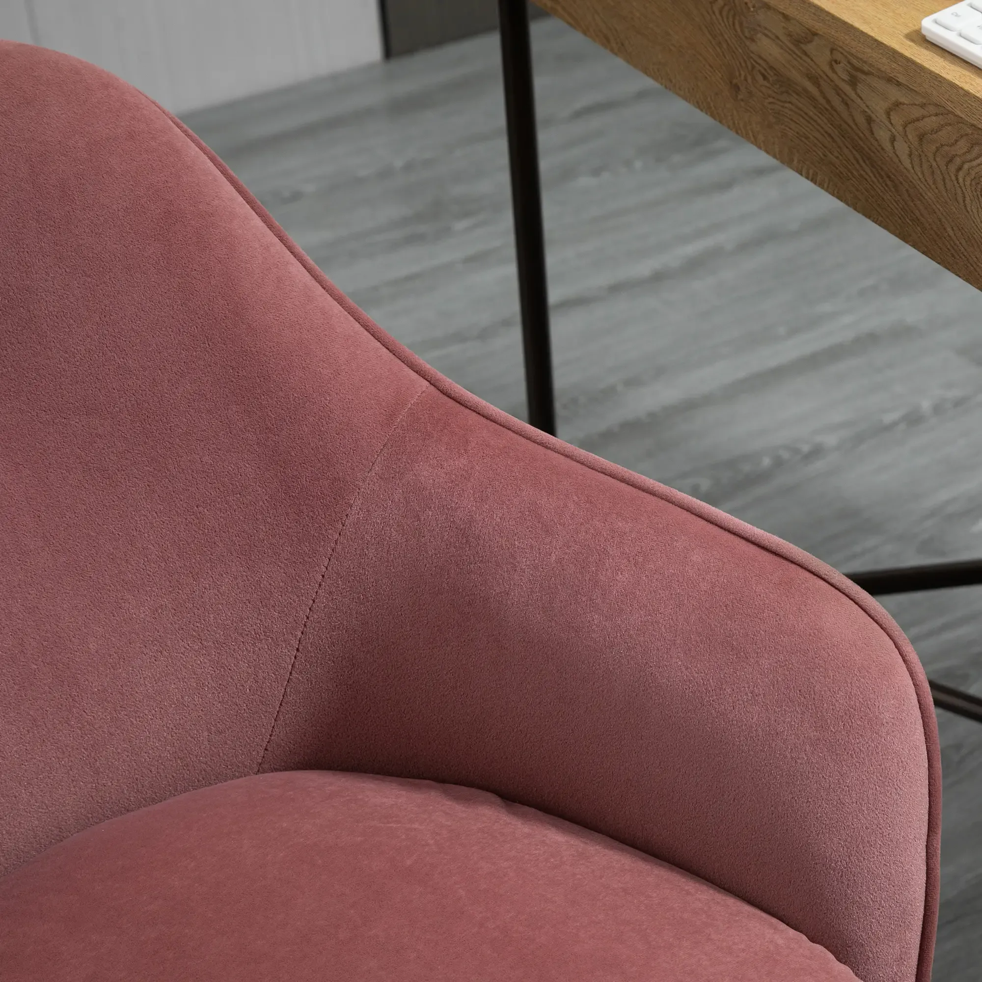 Nahaufnahme eines rosa Samtstuhls. Im Hintergrund sind ein Holzschreibtisch und eine Tastatur zu sehen.