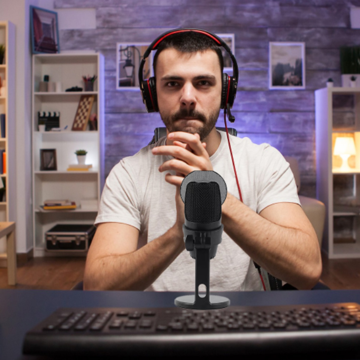 Mężczyzna z zestawem słuchawkowym i mikrofonem. Patrzy w kamerę. Tło obejmuje półki z książkami, klawiaturę i biurko.