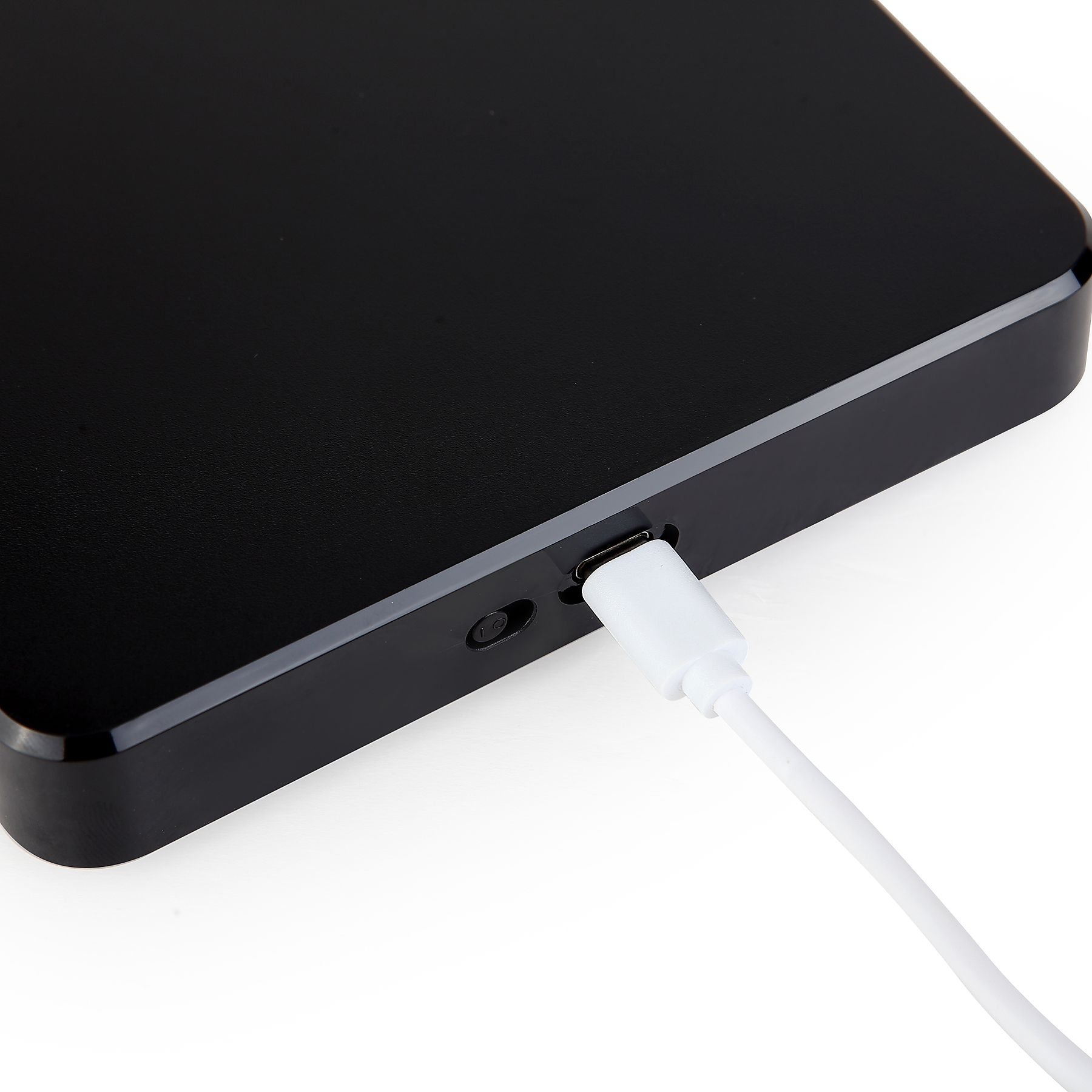 Ein schwarzes Gerät wird mit einem weißen Kabel geladen. Das Kabel ist auf weißem Hintergrund mit dem Gerät verbunden.