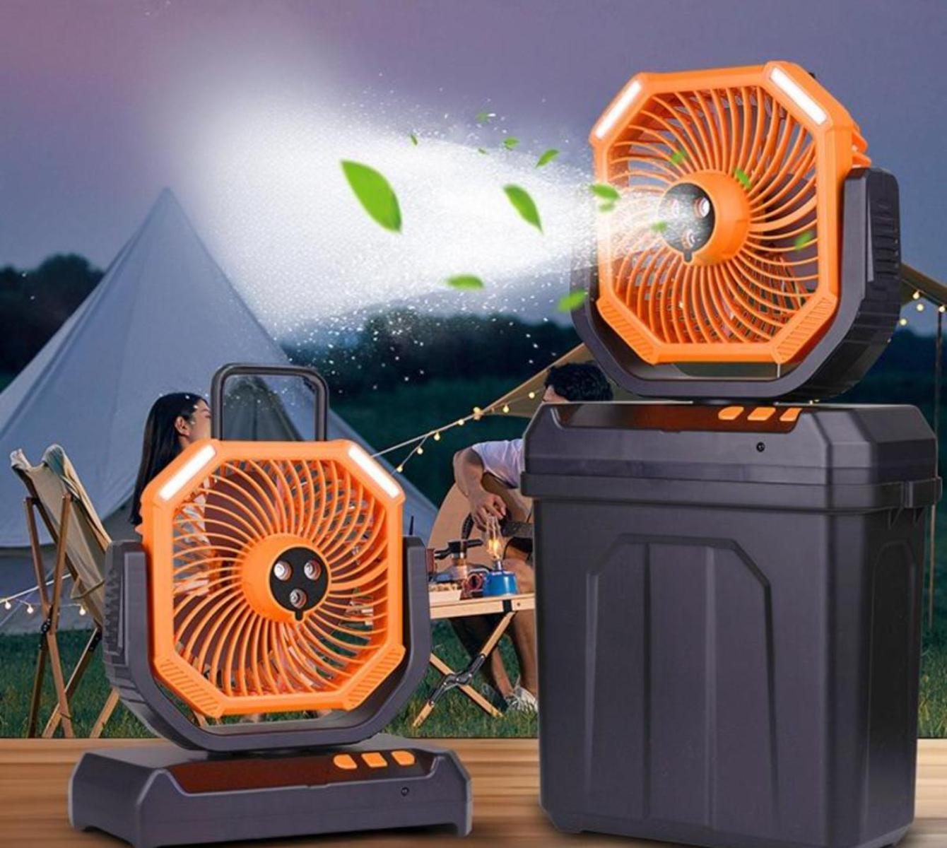 Zwei orangefarbene Ventilatoren mit Lichtern, einer auf einer Box, ein anderer auf einem Sockel. Im Hintergrund sind ein Zelt und Personen zu sehen, mit Blättern in der Luft.