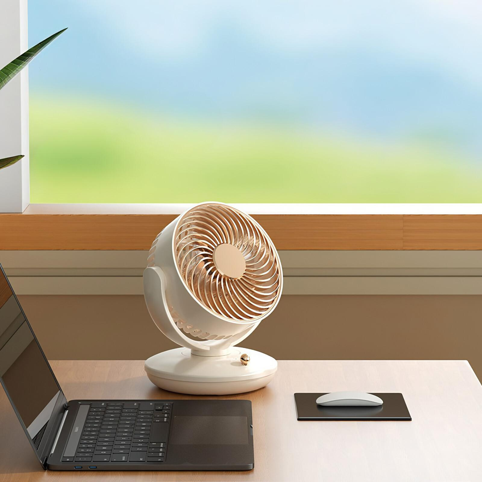 Ein weißer Schreibtischventilator steht auf einem Holztisch mit einem Laptop, einer Maus und einem Fenster mit grüner und blauer Aussicht.