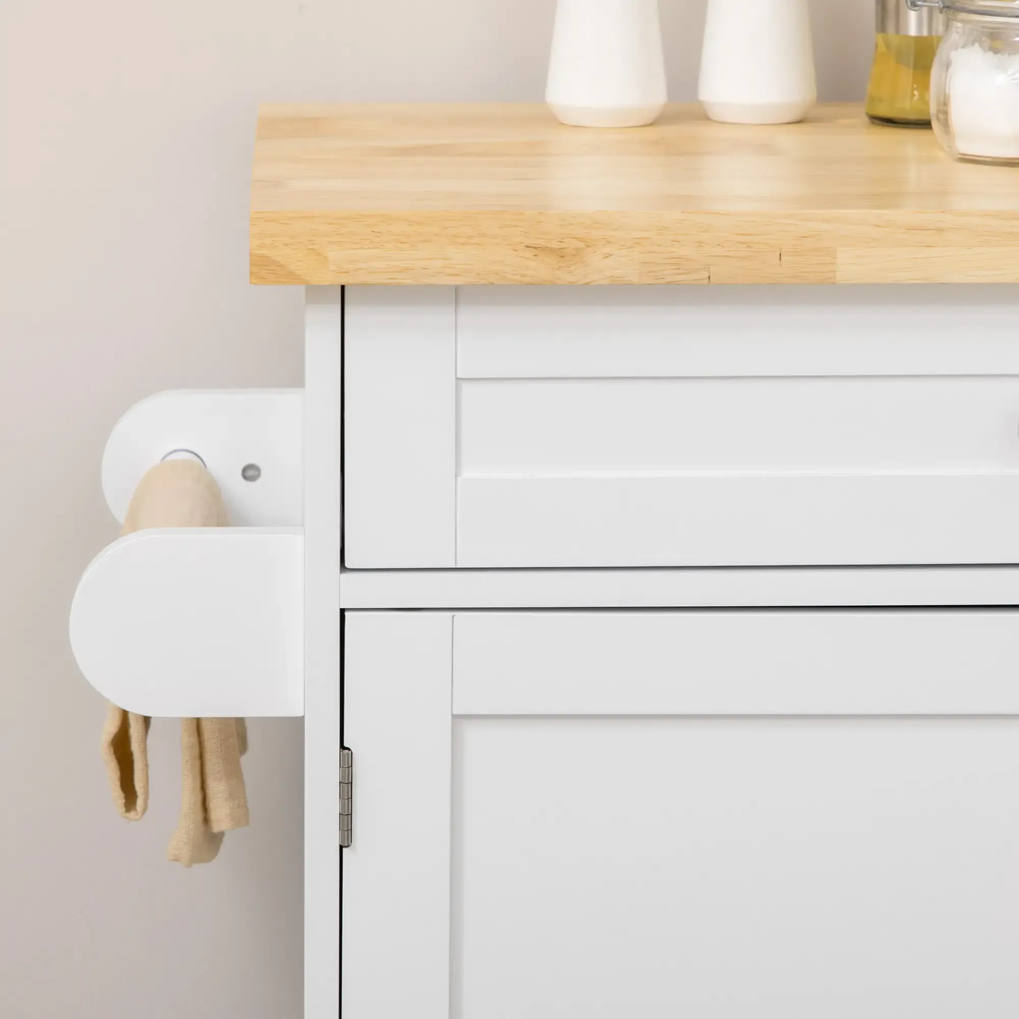 Ein weißer Schrank mit Holzplatte. Auf der Theke stehen zwei weiße Flaschen und Gläser. An der Seite hängt ein beiges Handtuch.