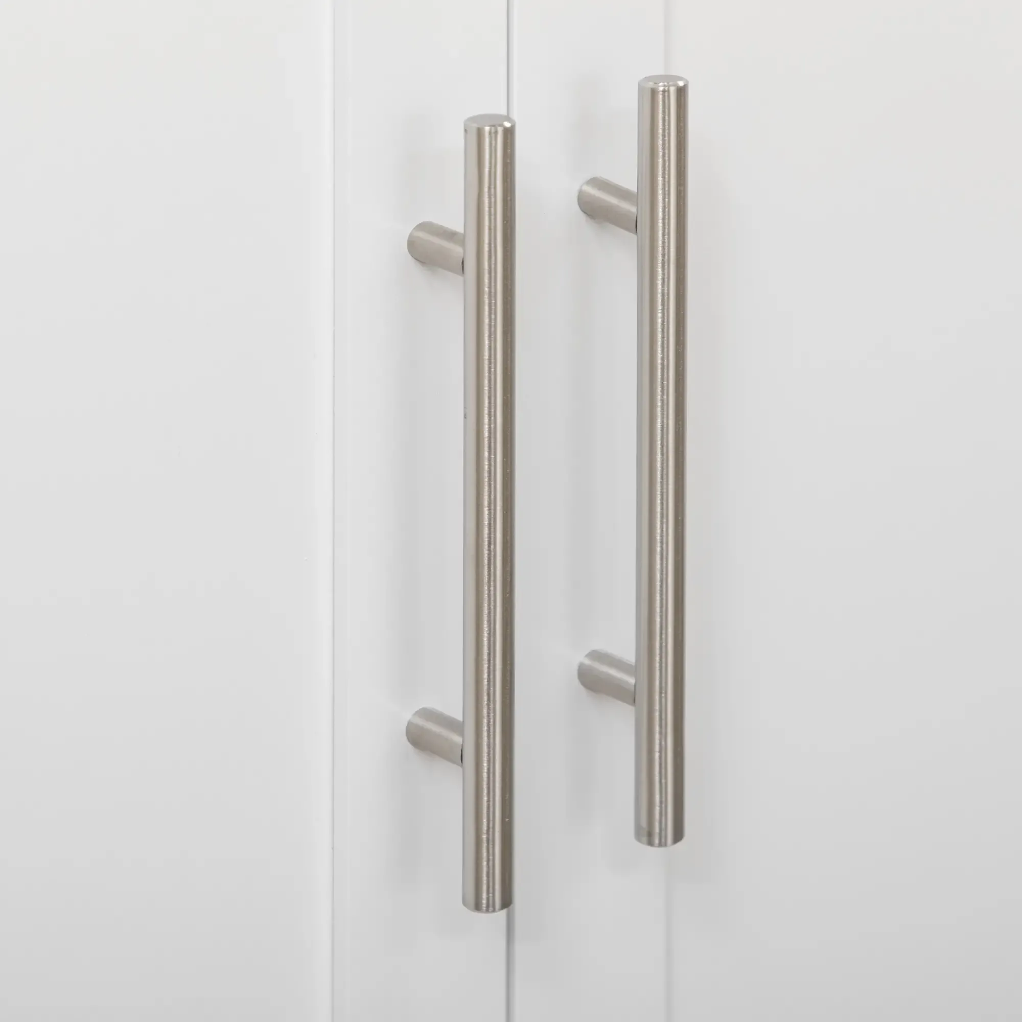 Nahaufnahme von zwei weißen Schranktüren mit vertikalen, silbernen Stangengriffen. Schlichtes und modernes Design.