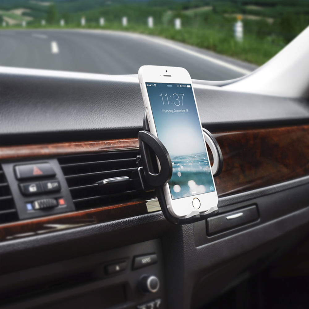Ein weißes Smartphone in einer Autohalterung zeigt 11:37 Uhr an. Das Armaturenbrett ist sichtbar. Eine Straße und grüne Hügel sind im Hintergrund.