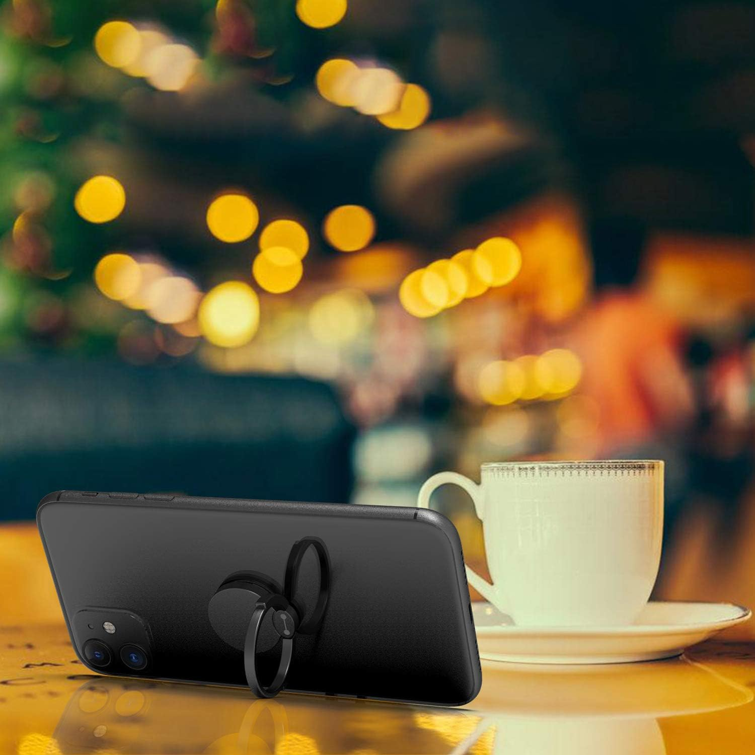 Ein schwarzes Telefon mit Ringhalter steht auf einem Tisch. Daneben steht eine Tasse Kaffee auf einer Untertasse, mit Bokeh-Lichtern im Hintergrund.