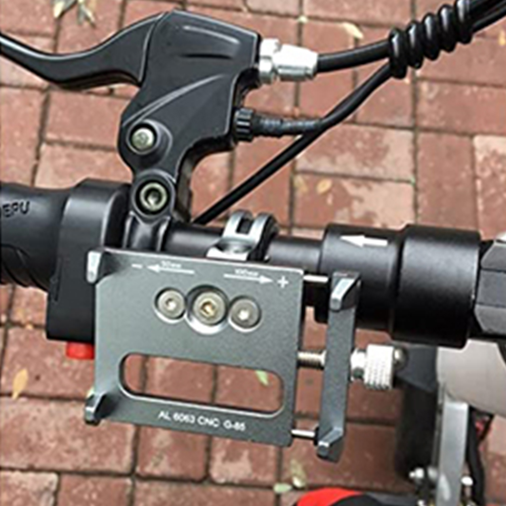 Nahaufnahme eines E-Scooter-Lenkers. Schwarzer Bremshebel, Telefonhalterung und Kabel sichtbar. Hintergrund ist Ziegelpflaster.