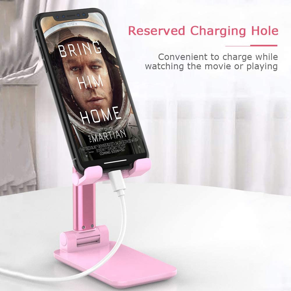 Ein pinkfarbener Telefonständer hält ein Telefon mit einem Filmplakat. Ein weißes Ladekabel ist eingesteckt. Text lautet "Reserviertes Ladeloch".