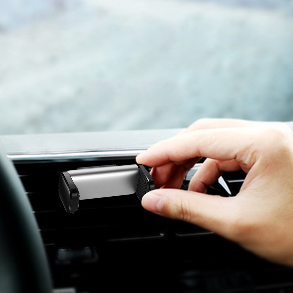Eine Hand platziert eine silberne und schwarze Autotelefonhalterung auf einer schwarzen Lüftungsöffnung in einem Auto. Der Hintergrund ist unscharf.