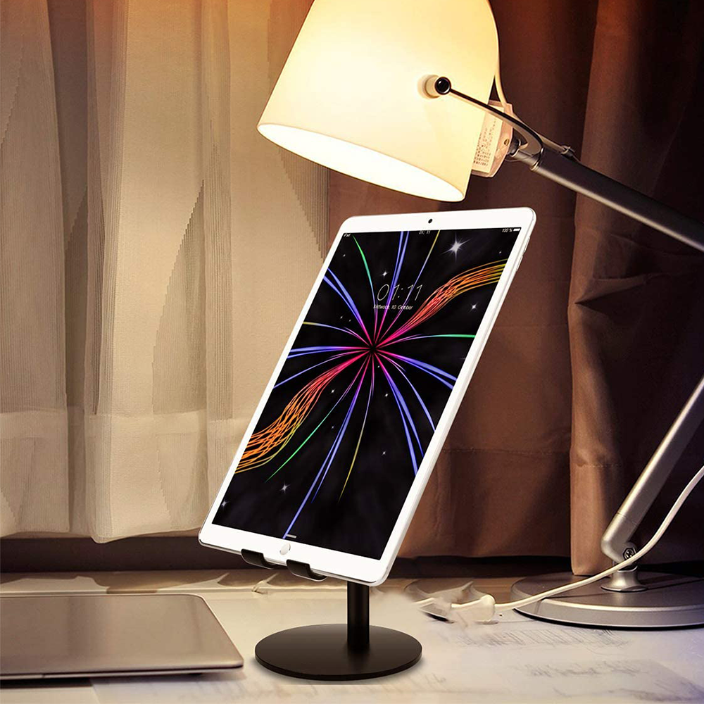 Ein Tablet mit bunten Feuerwerk-Anzeigen steht auf einem Ständer. Eine Schreibtischlampe befindet sich darüber, ein Laptop im Hintergrund.