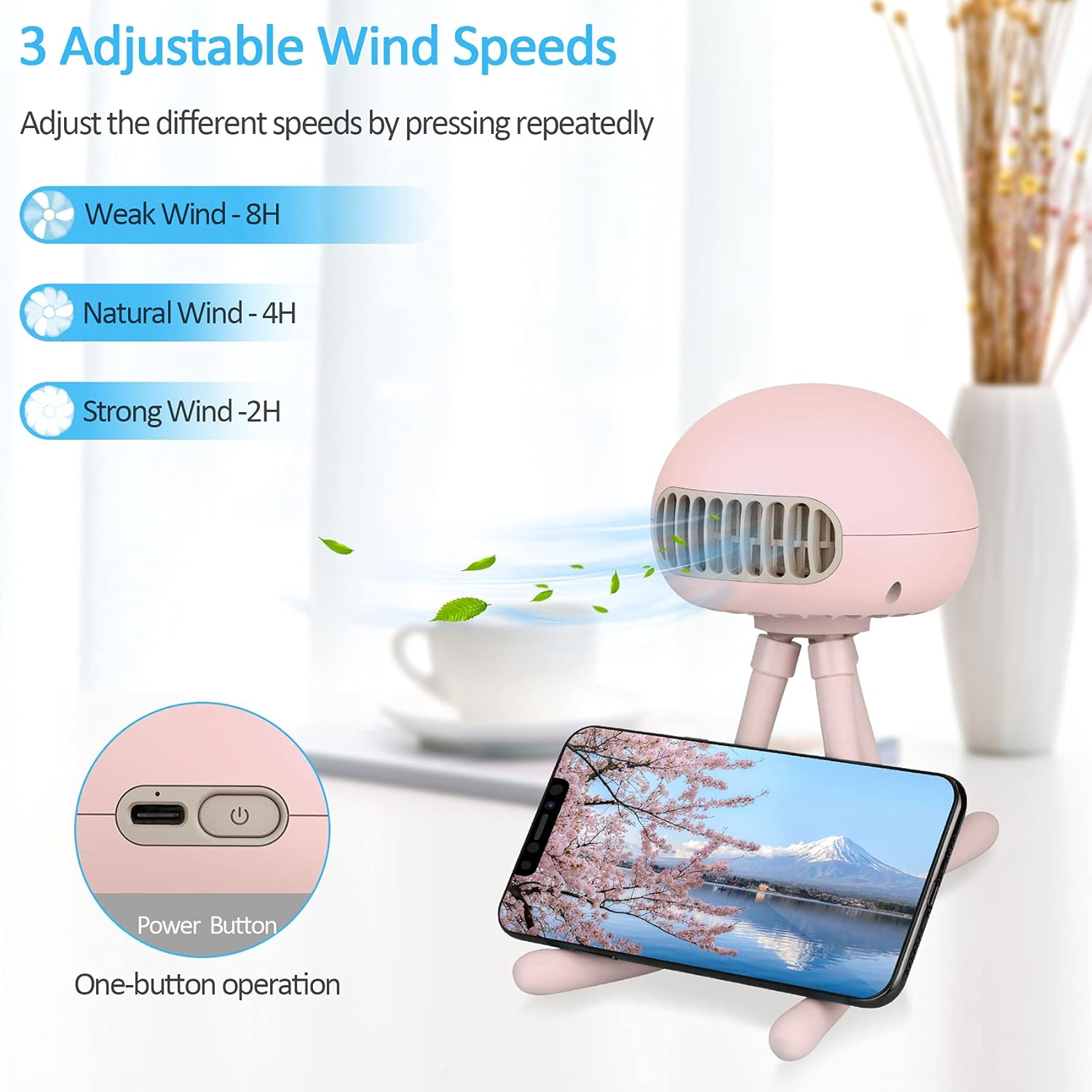 Ein rosa Ventilator mit einem Telefon, das eine Bergansicht zeigt. Der Ventilator hat drei Windgeschwindigkeitsoptionen. Eine Vase mit Blumen befindet sich im Hintergrund.