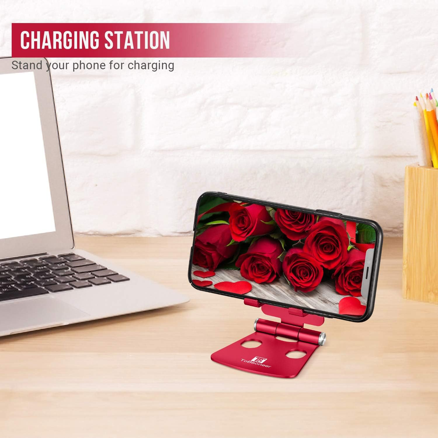 Ein Telefon auf einem roten Ständer zeigt Rosen. Ein Laptop und Bleistifte in einem Halter stehen auf einem Holzschreibtisch.
