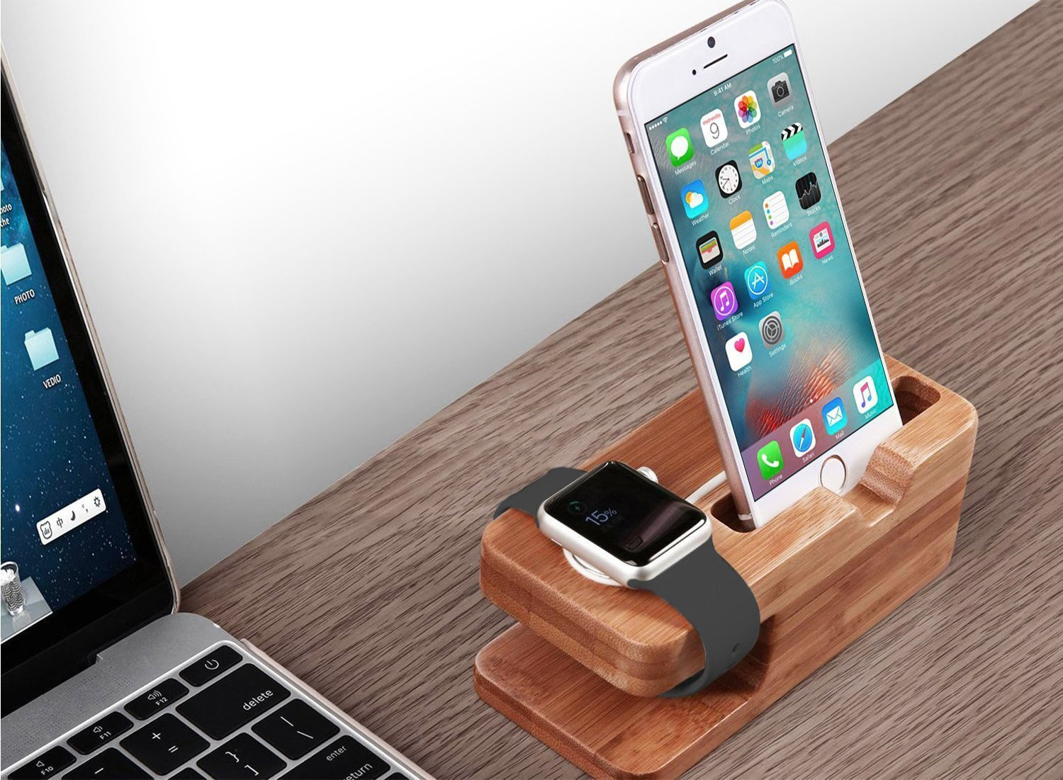 Ein iPhone und eine Apple Watch auf einem Holzständer. Im Hintergrund ein Laptop auf einem Holztisch.