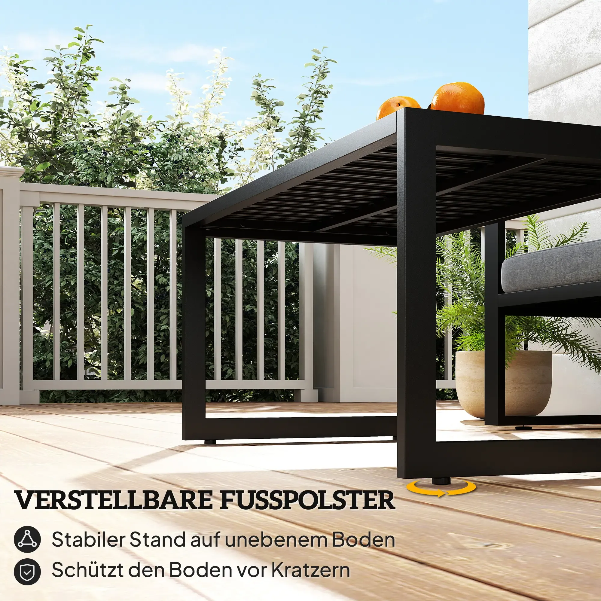 Schwarzer Metalltisch mit Orangen auf einer Holzterrasse mit Pflanzen und weißem Zaun im Hintergrund unter blauem Himmel.