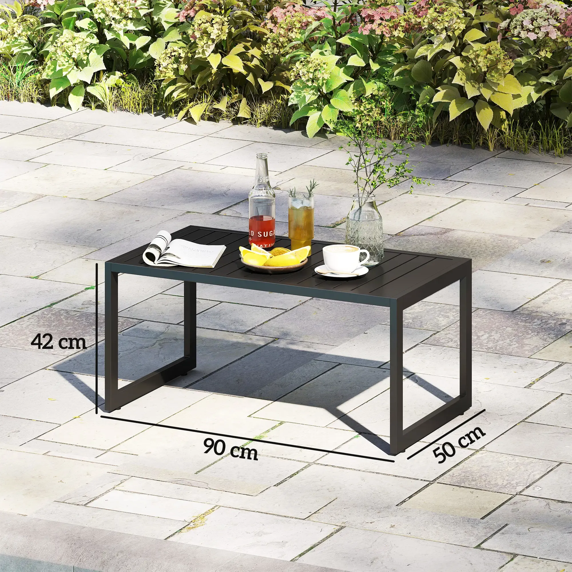 Ein schwarzer Tisch mit Getränken, Zitronen und einer Kaffeetasse steht auf einer Terrasse. Grüne Pflanzen sind im Hintergrund.