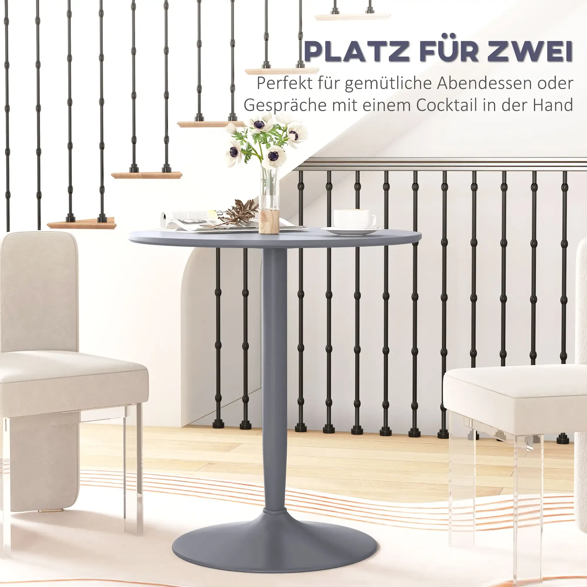 Kleiner Tisch mit Blumen, Kaffeetasse und zwei Stühlen. Im Hintergrund Treppen und ein schwarzes Geländer.