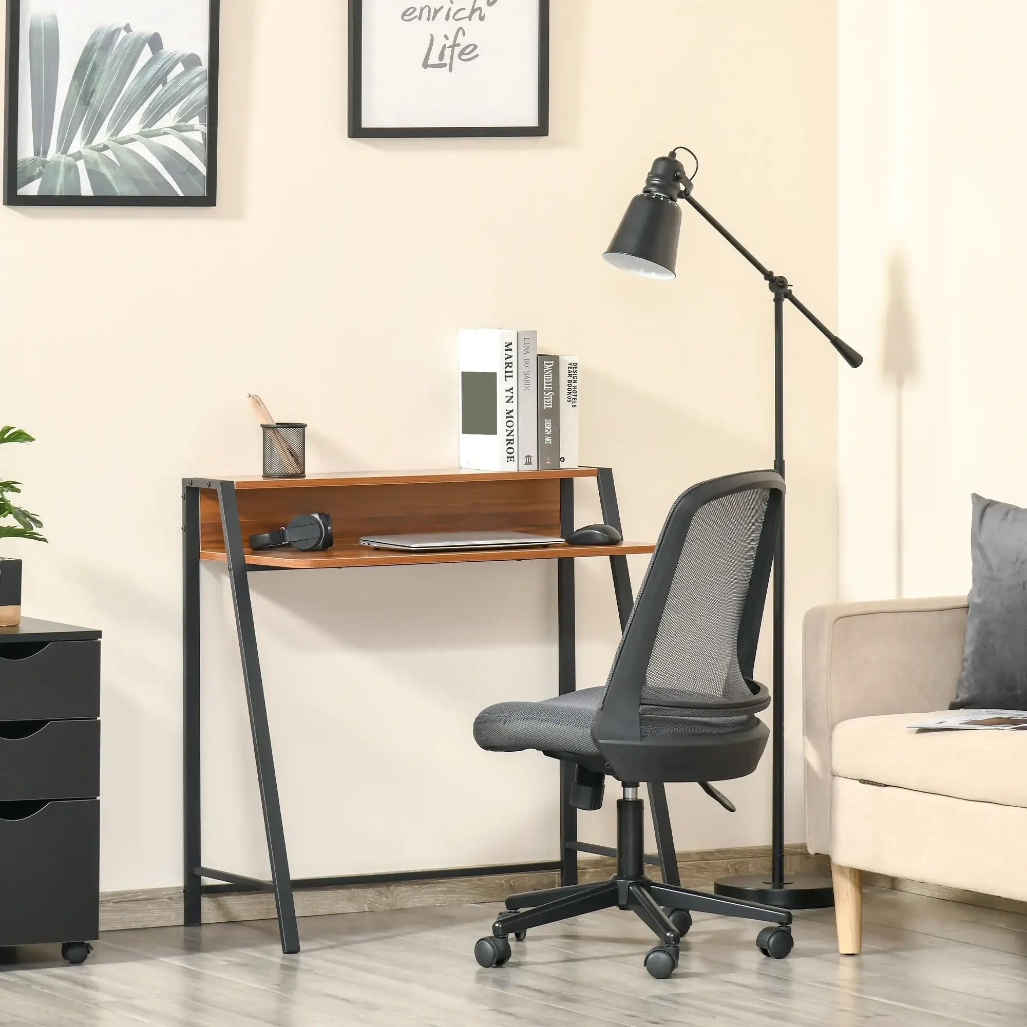 Ein Schreibtisch mit Laptop, Büchern und Stuhl. Im Hintergrund eine Lampe und ein Sofa. Die Wände sind beige.