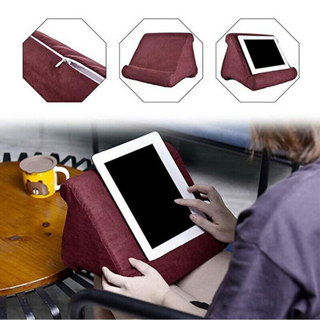 Eine Person hält ein Tablet auf einem weinroten Kissen. Das Tablet ist schwarz. Auf einem Tisch steht eine Tasse.